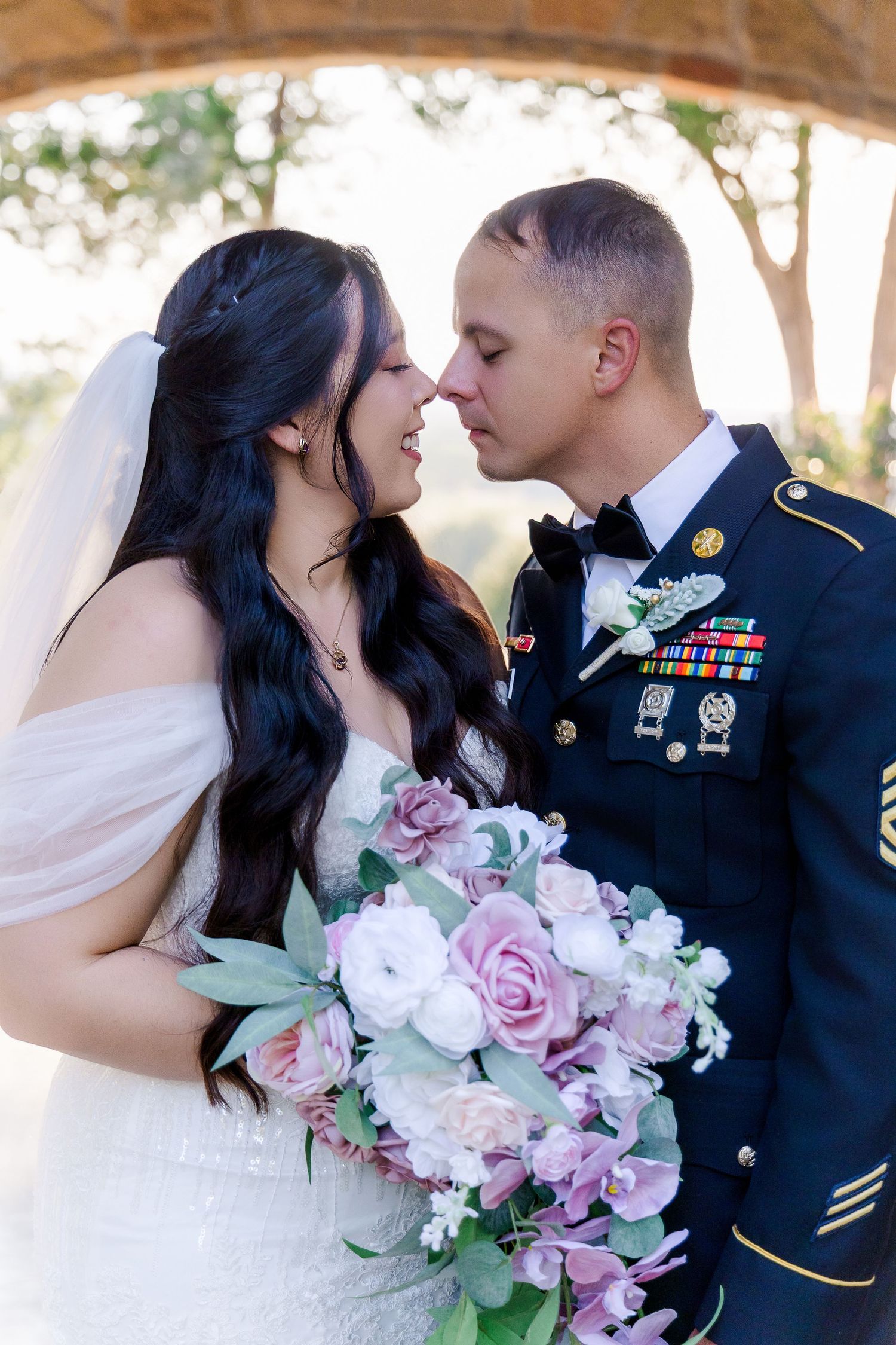 A romantic wedding moment with a bride in white holding pink roses and a groom in military dress uniform.