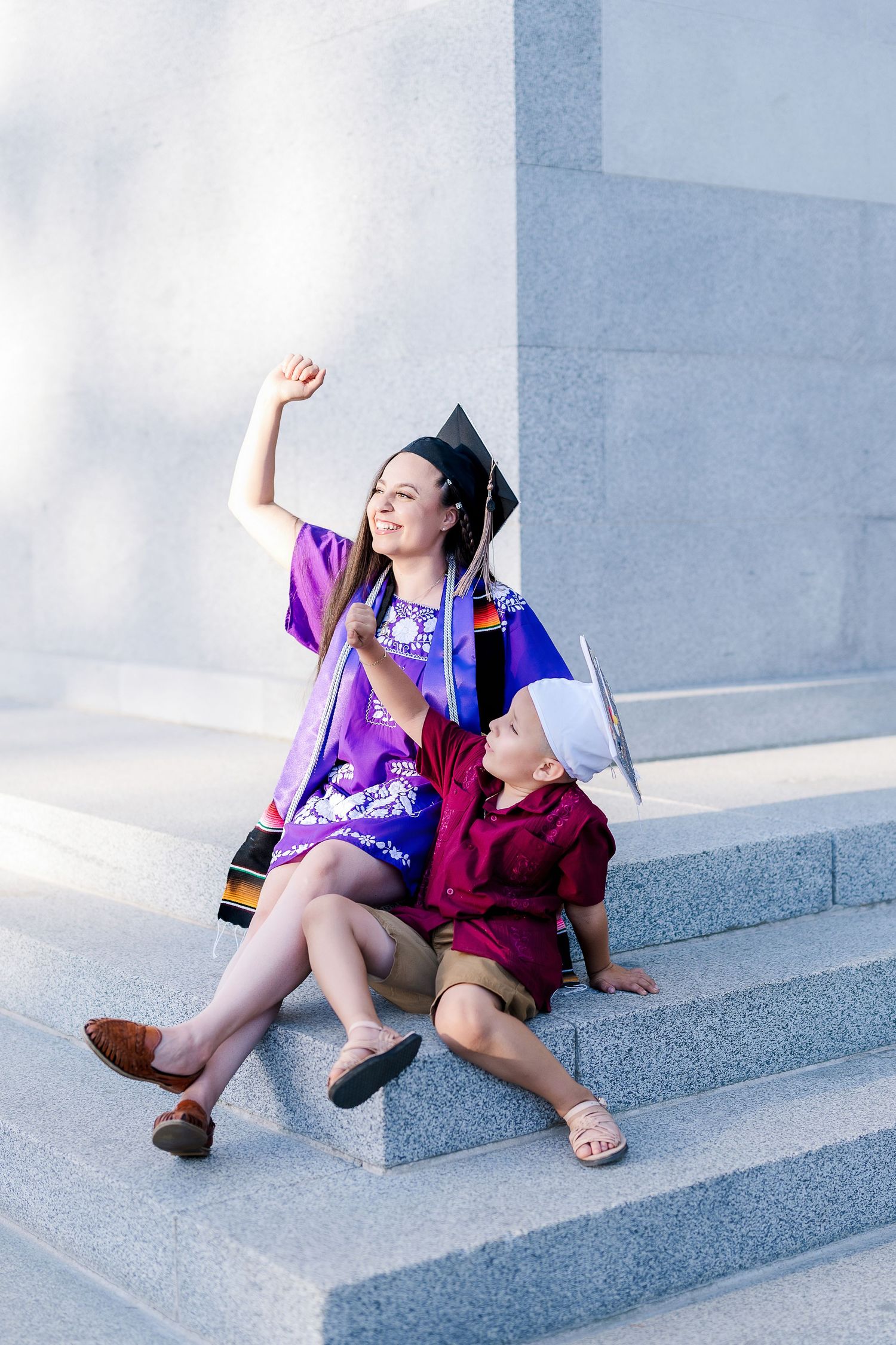 Two people in purple and maroon outfits sitting playfully on grey concrete steps.