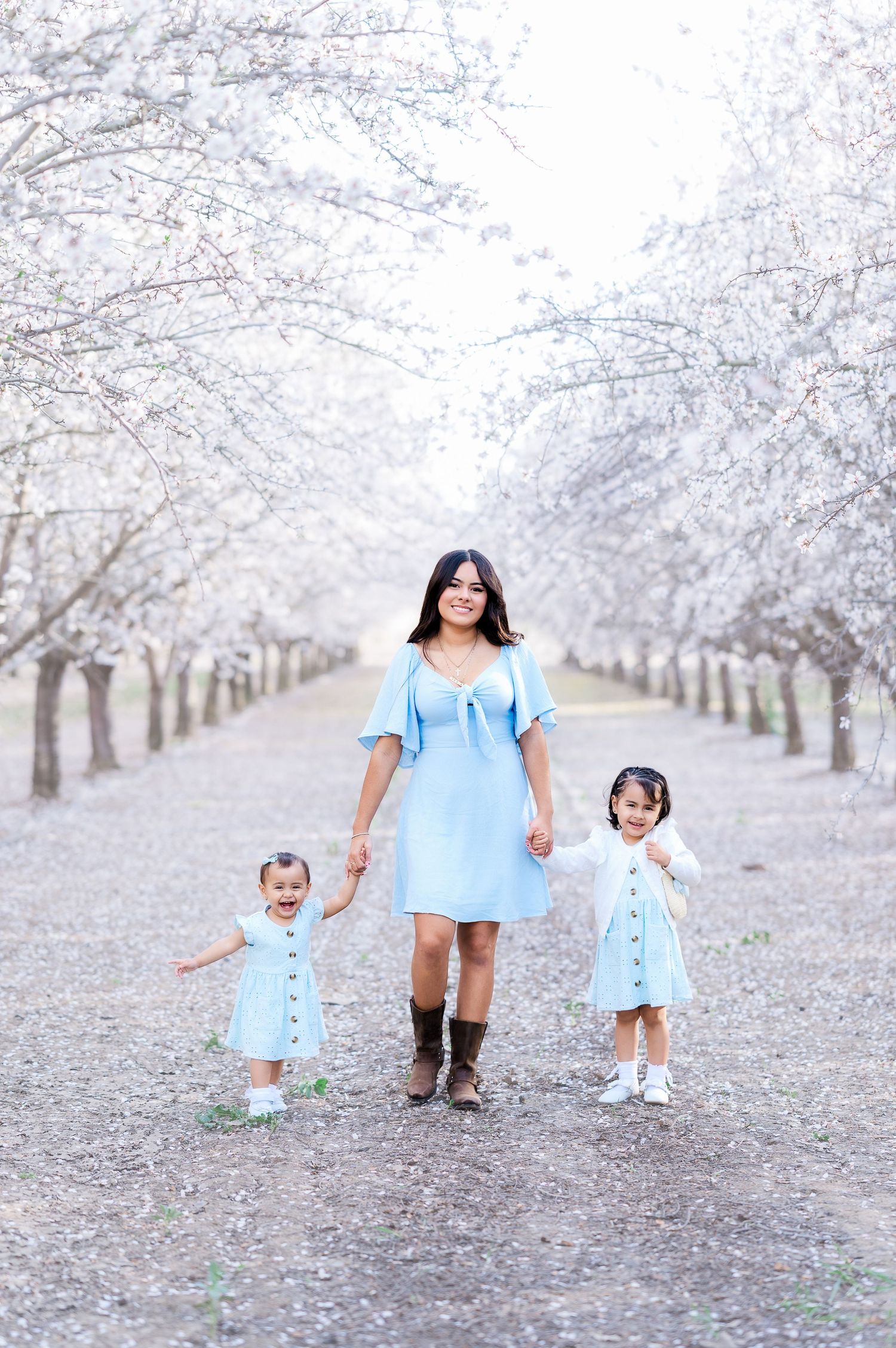 Family wearing matching blue dresses walks together through a beautiful almond blossom orchard on a spring day.