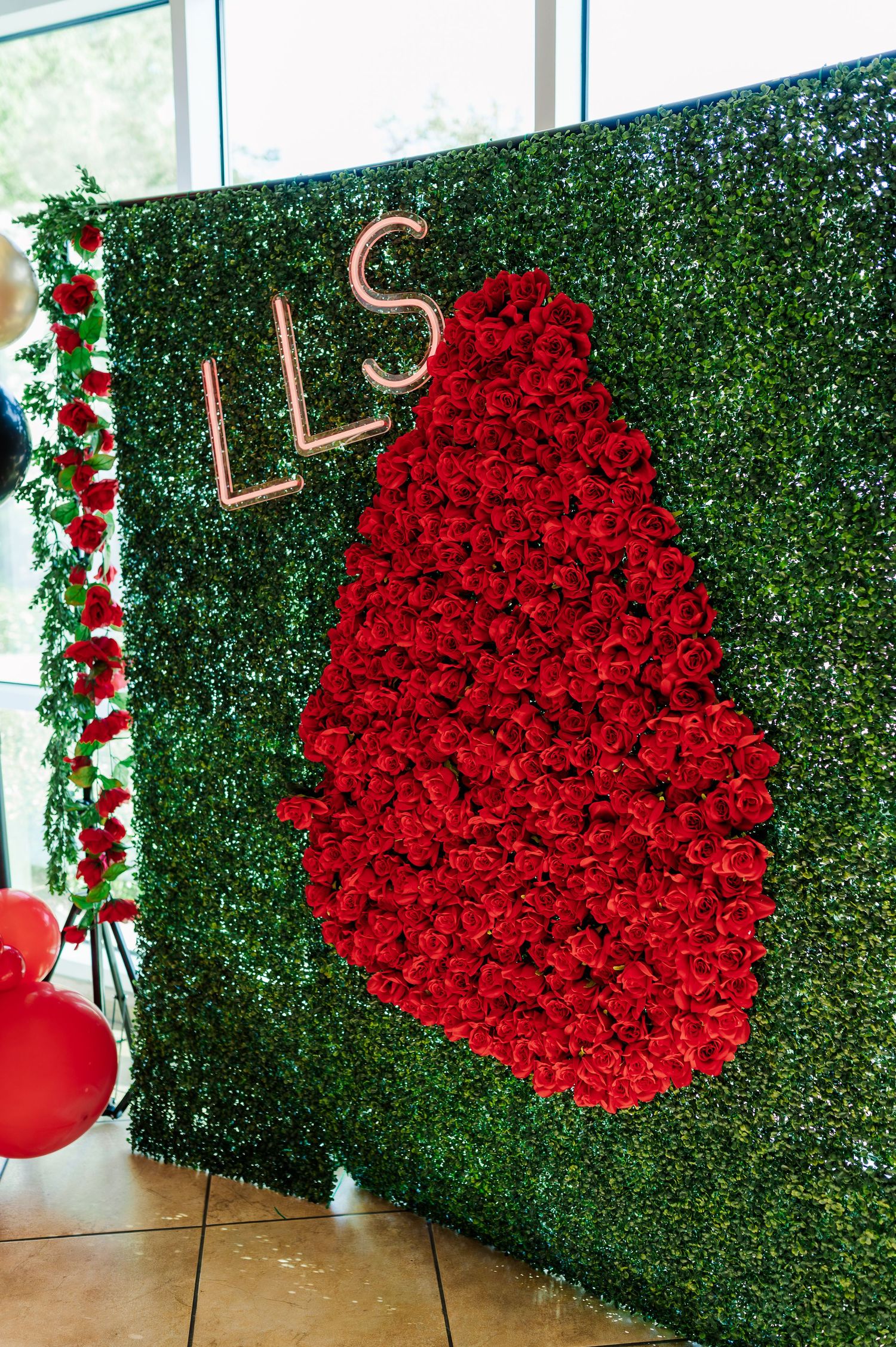 Heart-shaped red rose wall display against green hedge backdrop with decorative elements for romantic events.