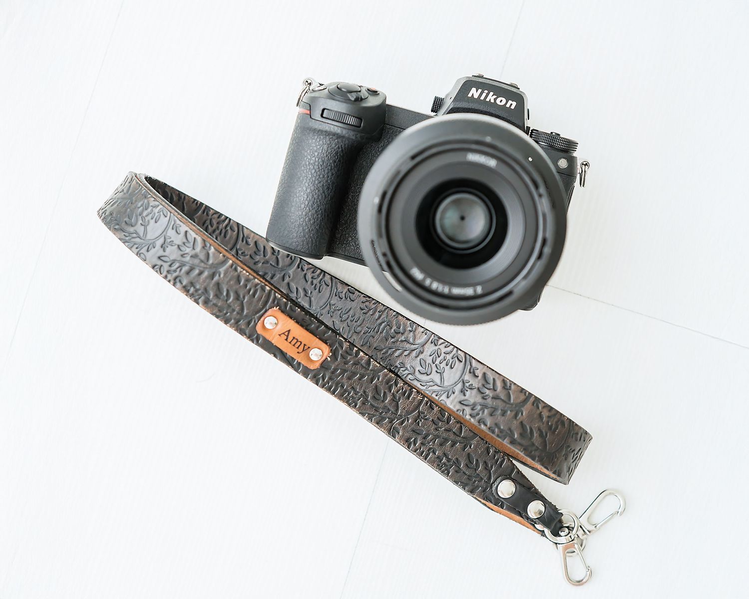 Nikon mirrorless camera with textured leather camera strap on white background.