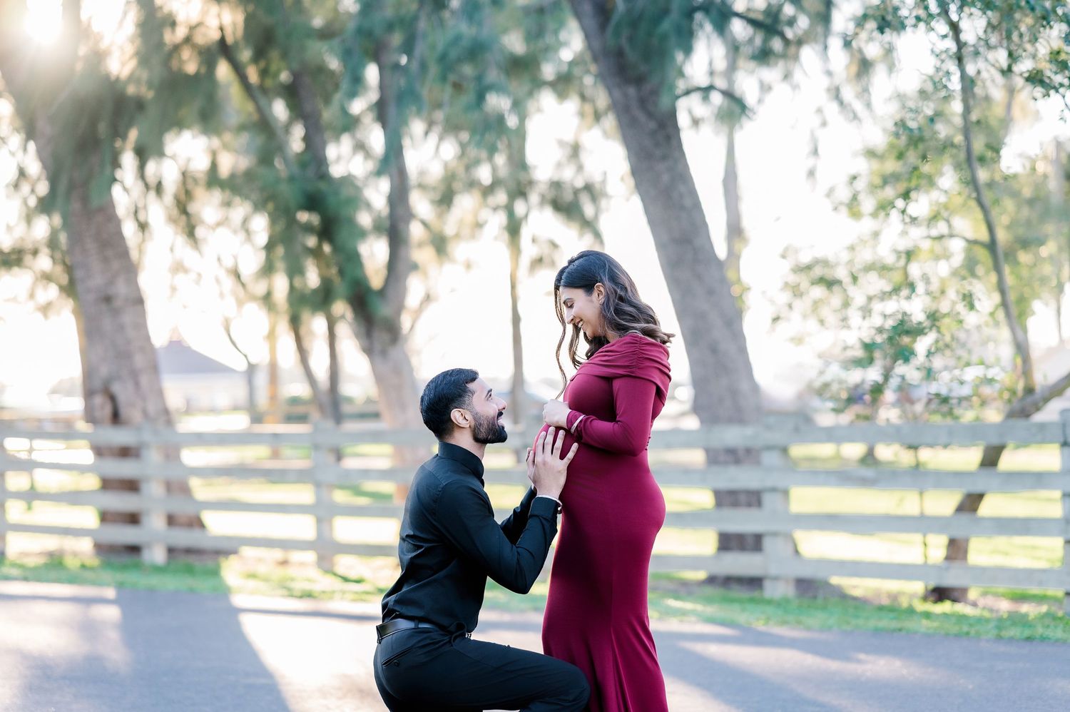 A couple dancing together in a sunny park surrounded by trees and white fences.