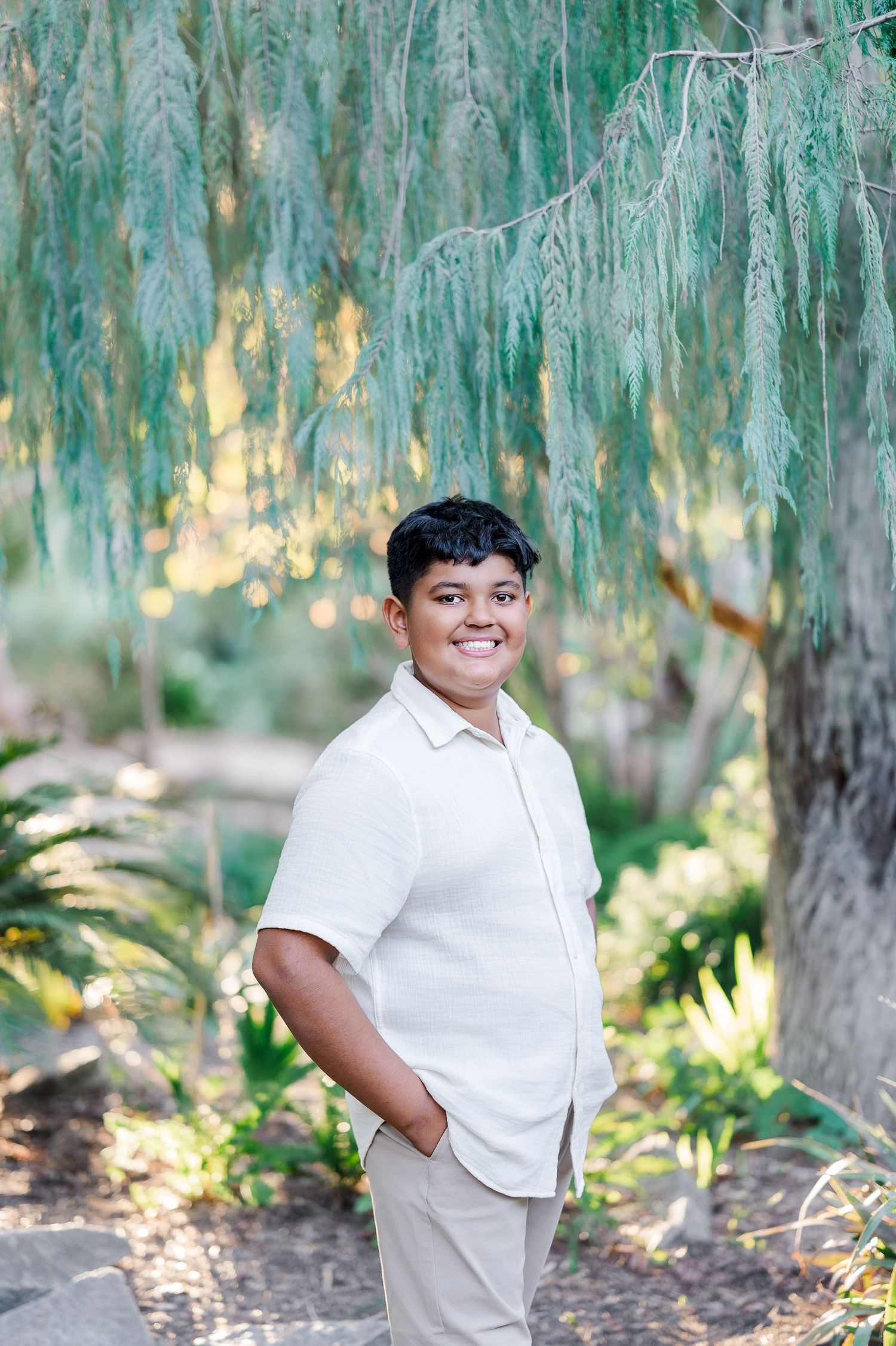 Outdoor portrait session under weeping willow trees with natural lighting and greenery.