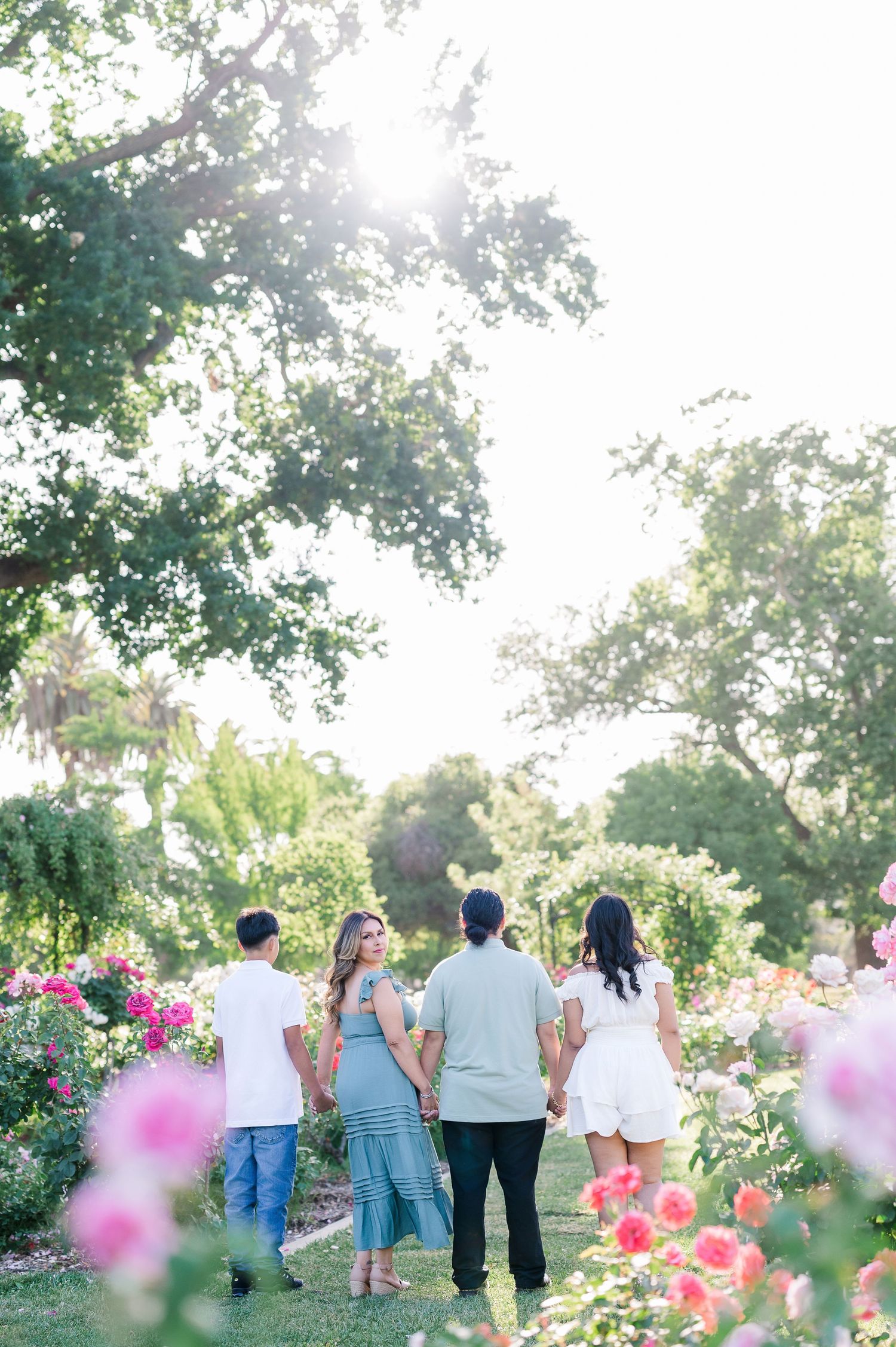 A group walks together through a lush garden with blooming pink flowers and sunlit trees in the background.