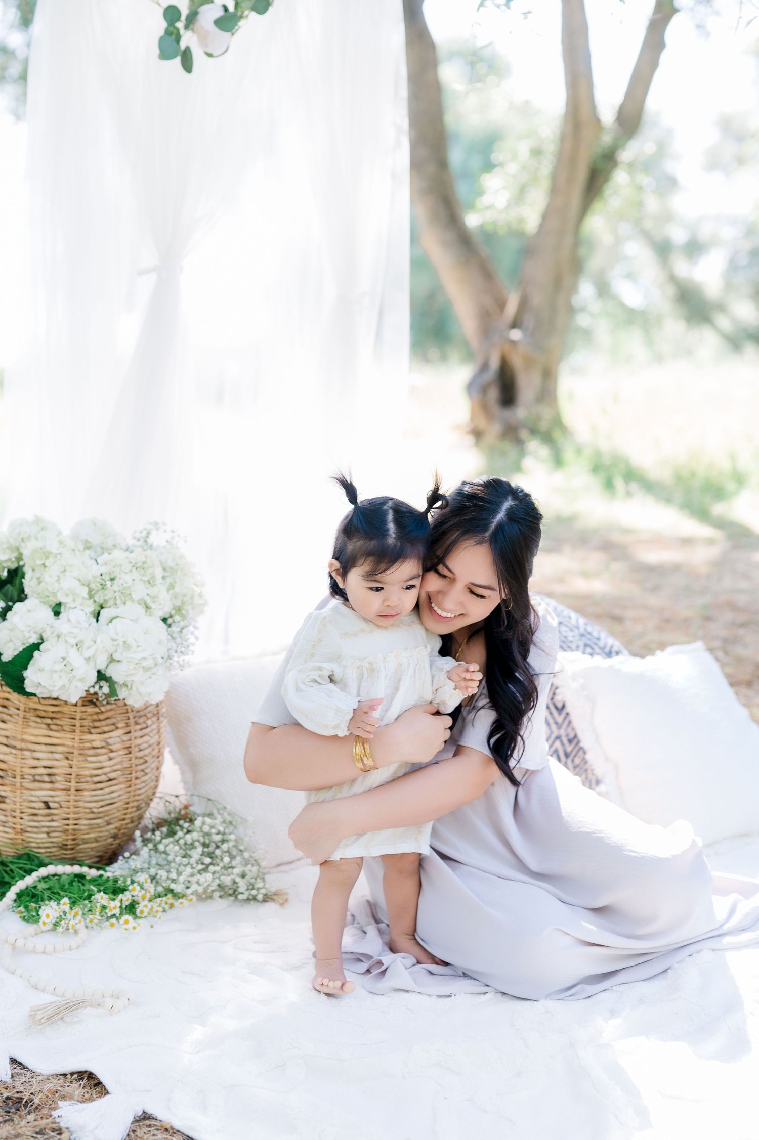 Tender outdoor maternity photoshoot featuring white dresses and floral arrangements in a dreamy garden setting.