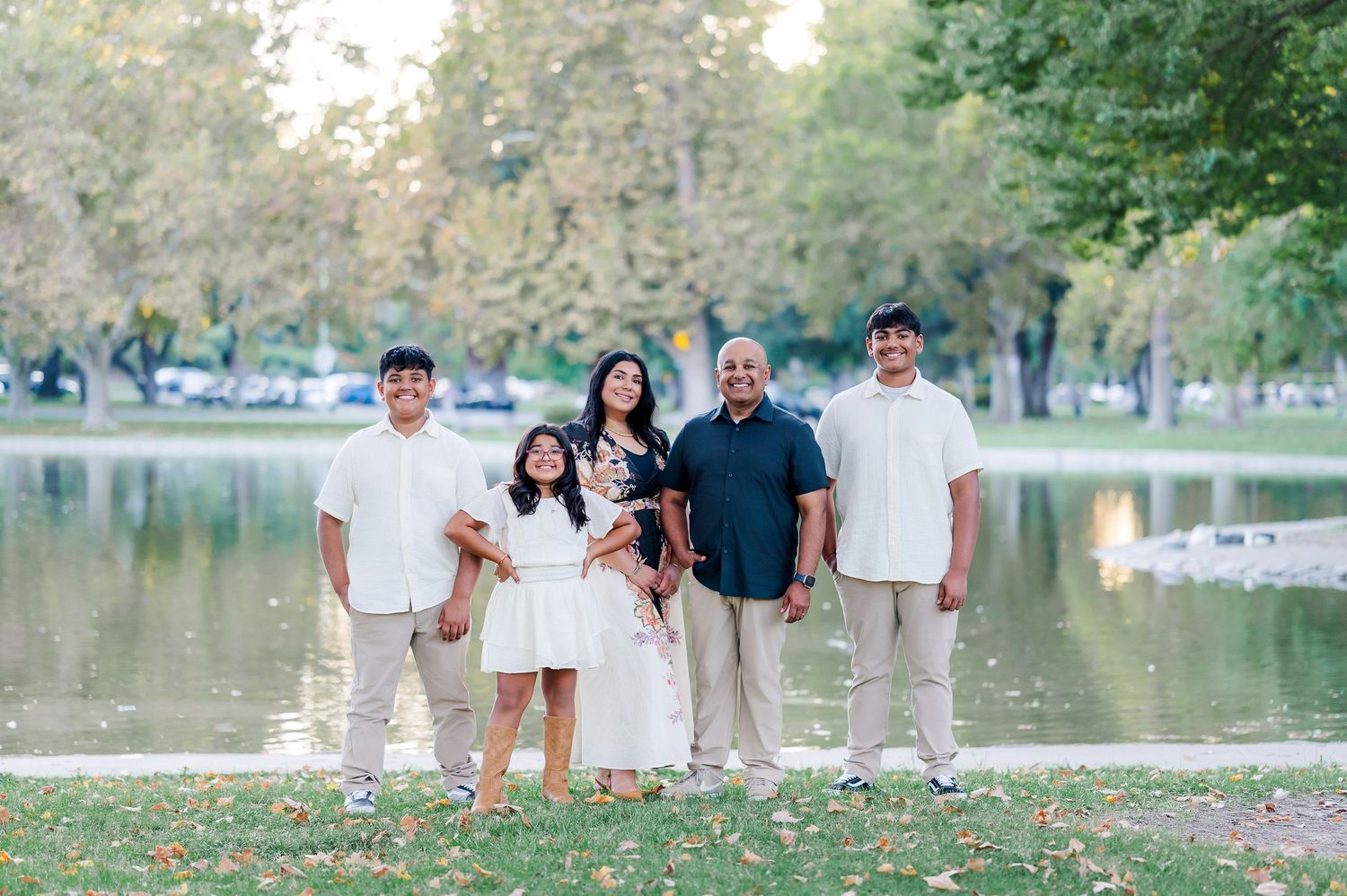 Family of five posing together by a serene park lake surrounded by lush green trees.