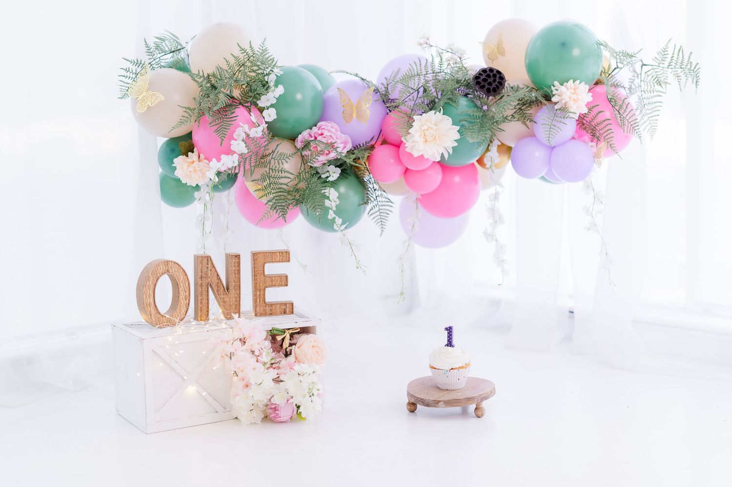 Colorful first birthday balloon garland with pink, mint, and purple balloons above a smash cake and ONE sign.