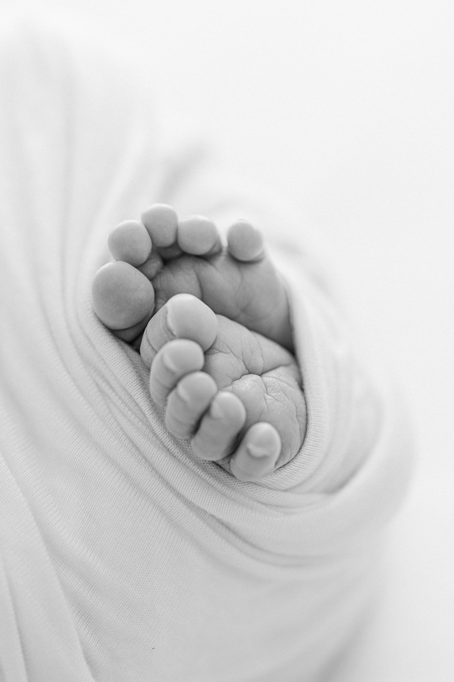 Black and white close-up photo of a newborn baby's tiny feet wrapped in soft white fabric.