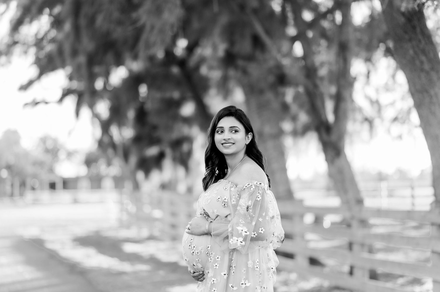 Black and white maternity portrait under trees with soft natural lighting.