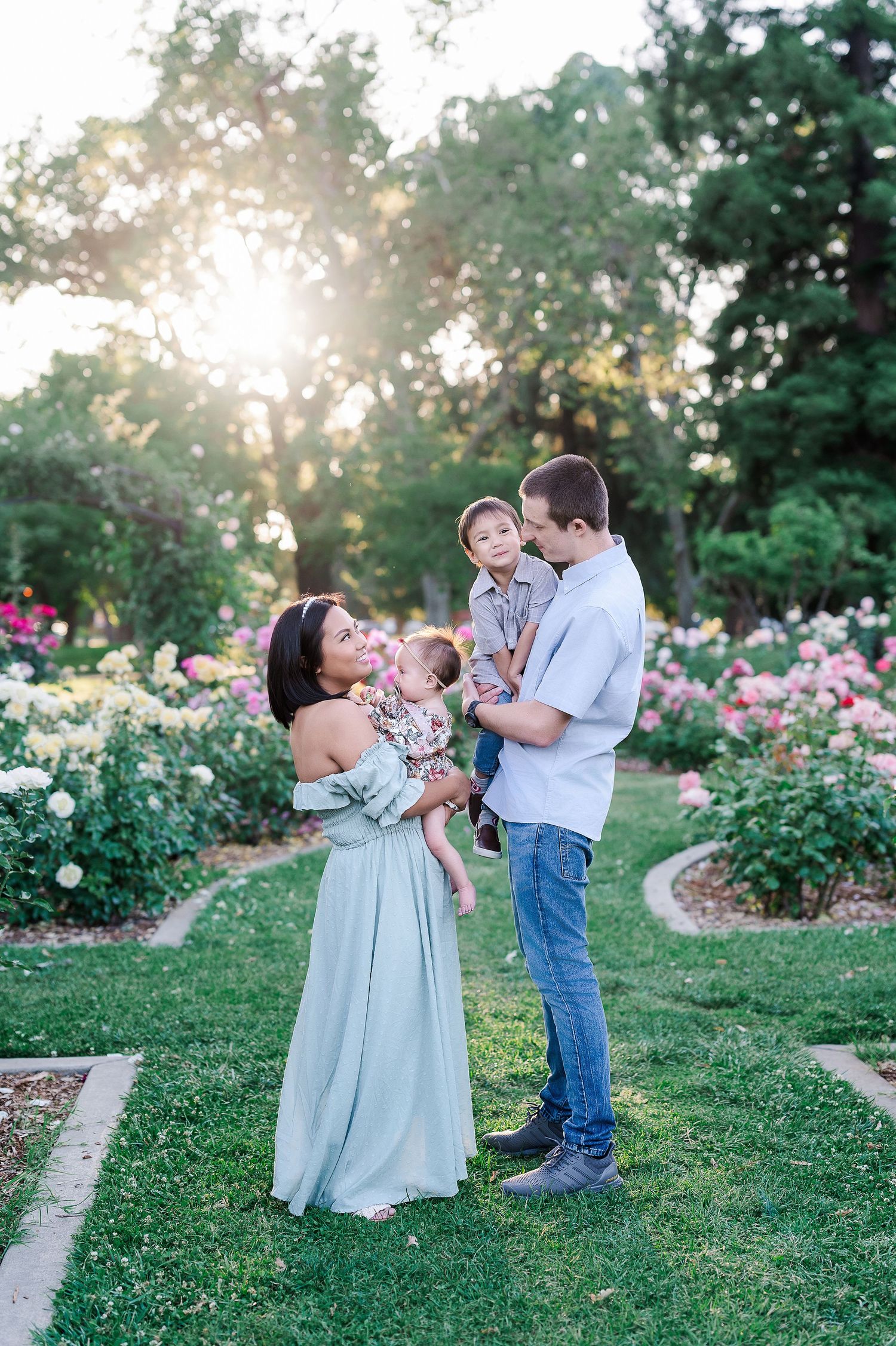 Family with young children in rose garden at sunset wearing coordinated pastel outfits.