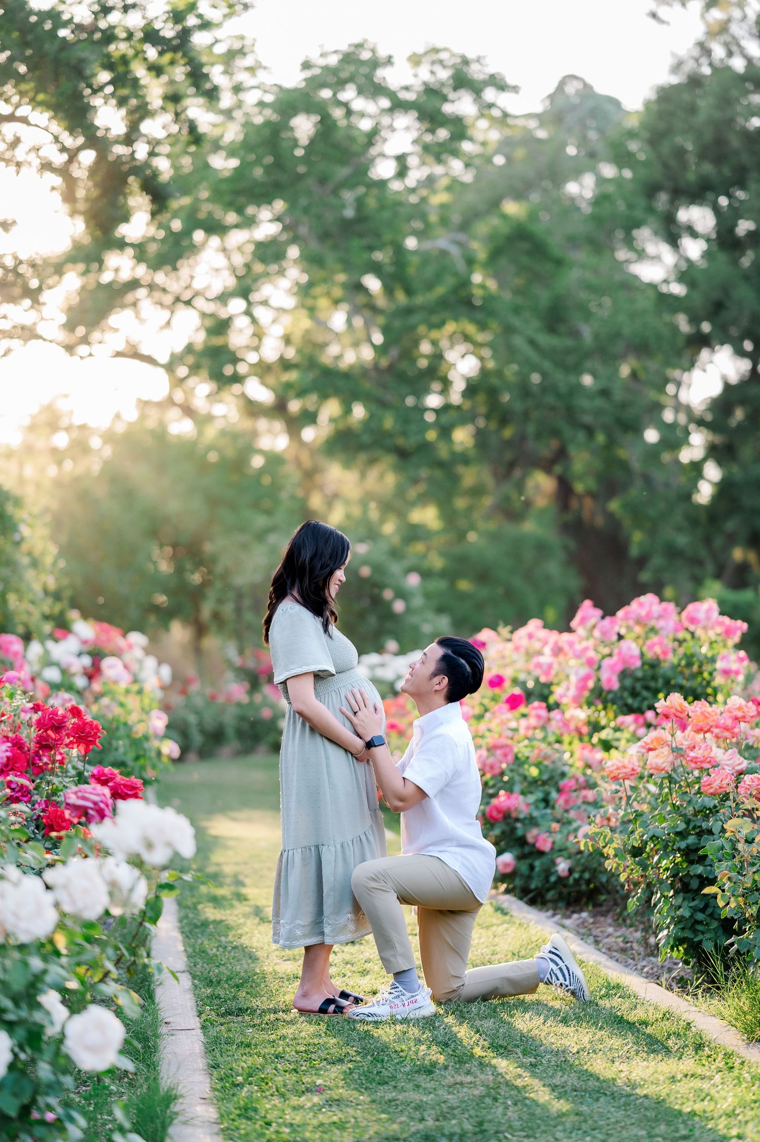 A couple shares a tender moment in a garden filled with blooming pink roses during golden hour.