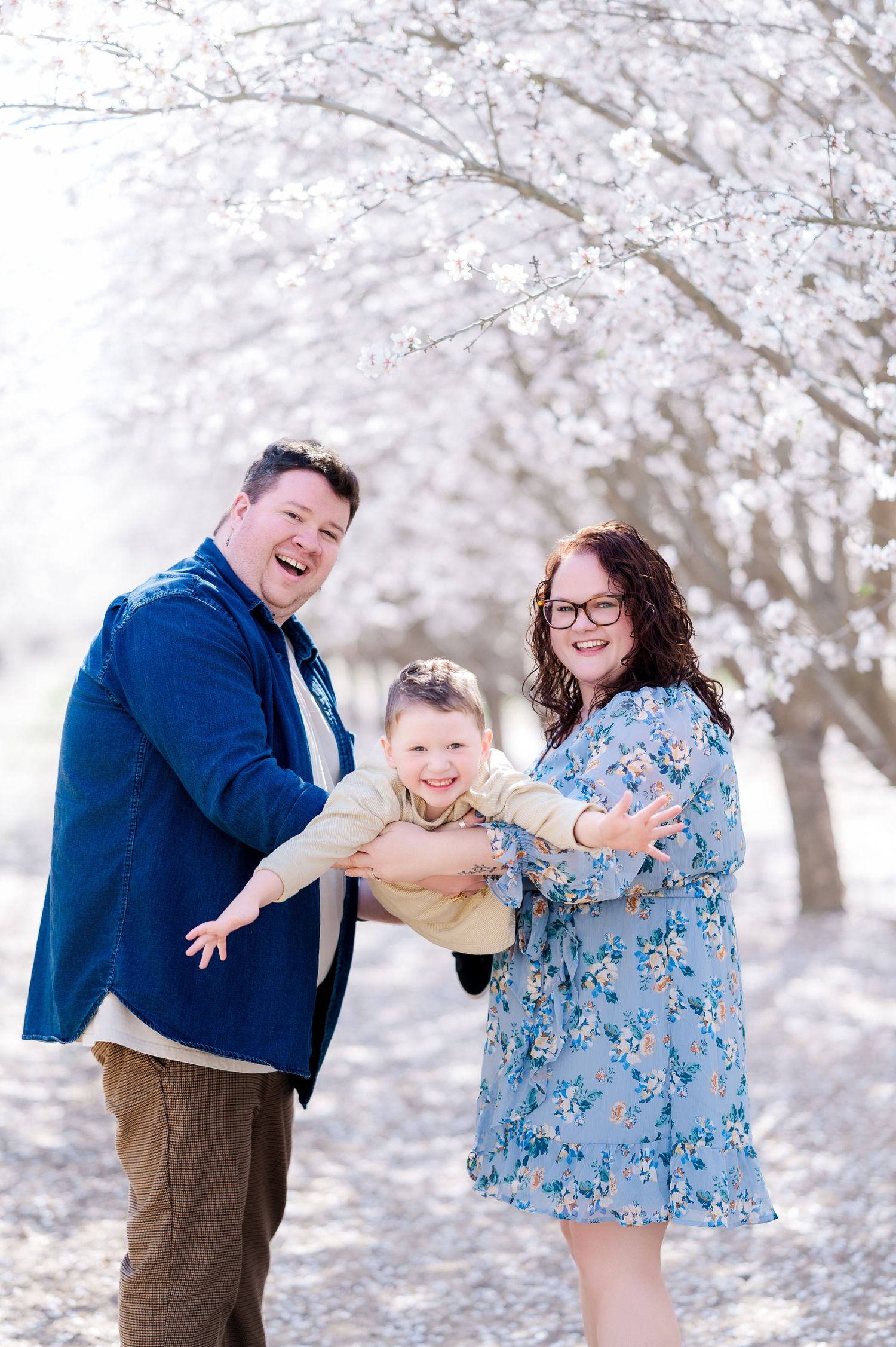 Playful couple dancing and twirling together in a dreamy winter scene with snow-covered cherry blossom trees.