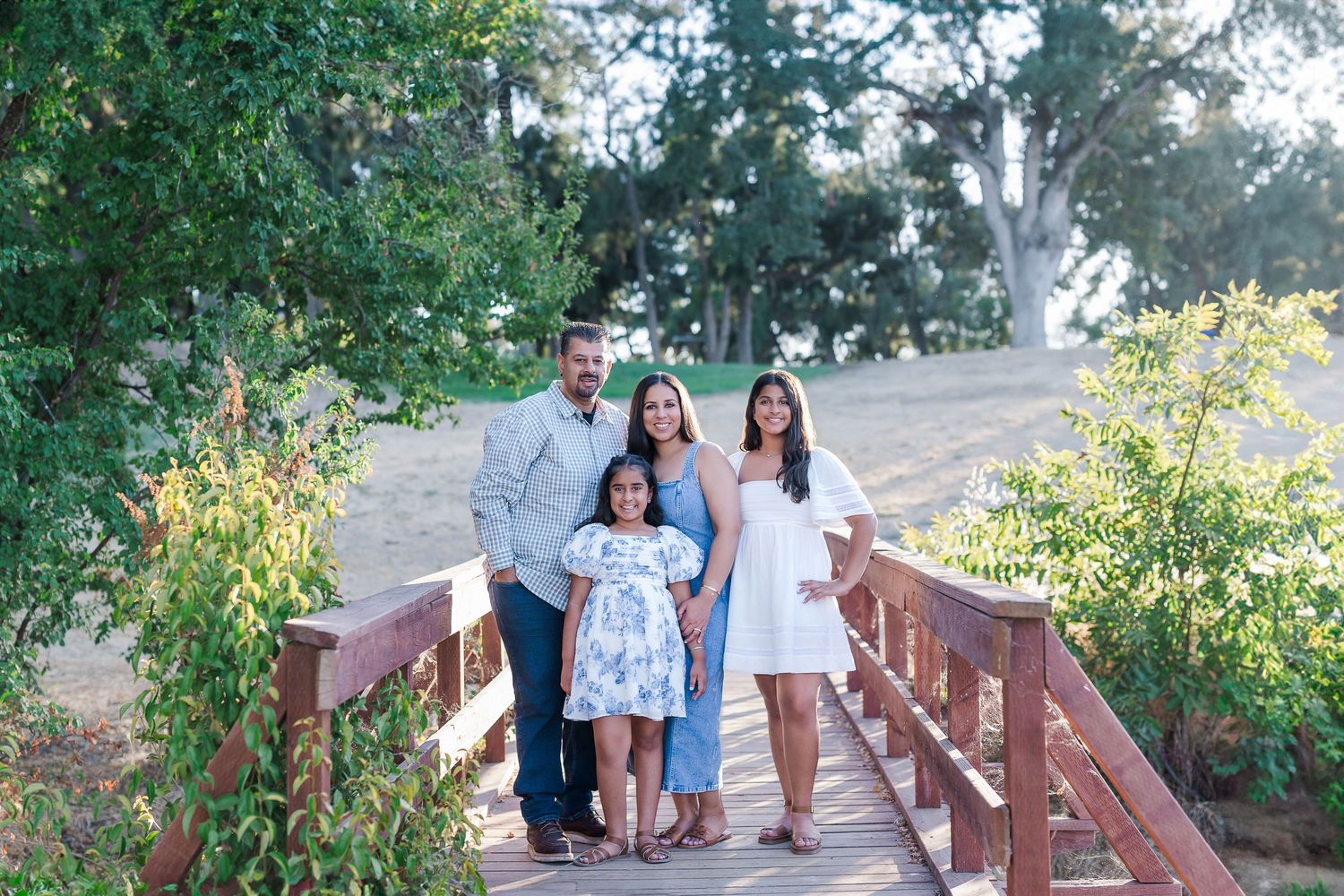 Family walking together on wooden bridge path surrounded by lush greenery.
