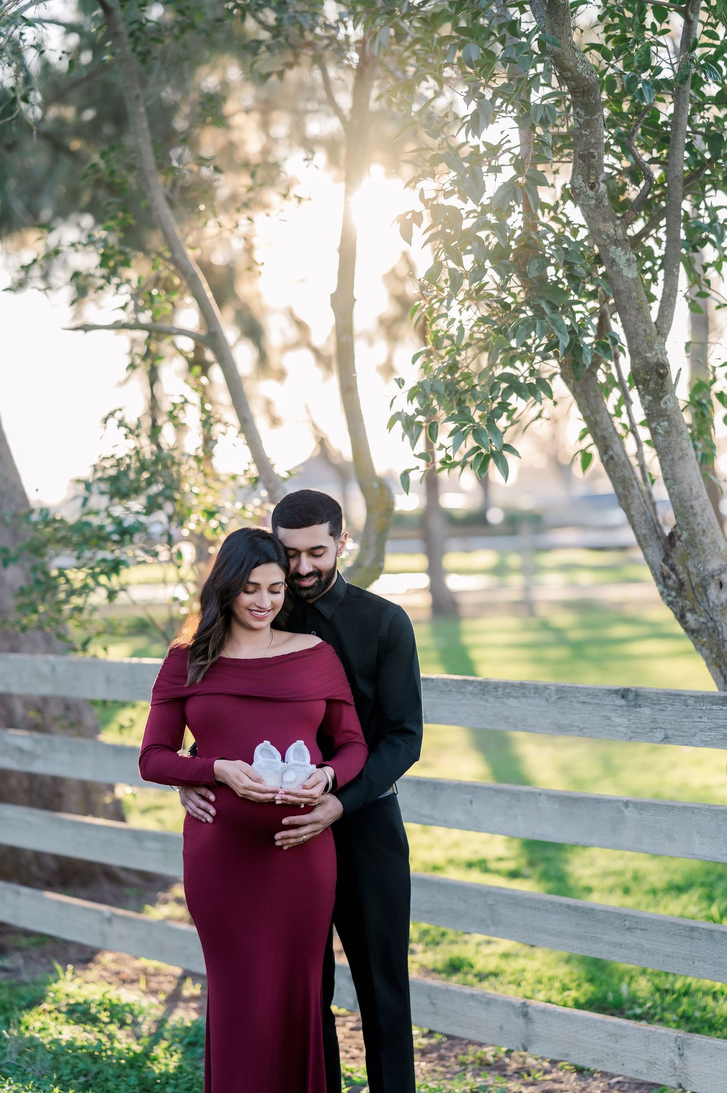 Couple poses together in a romantic outdoor maternity photoshoot among trees and sunlight.