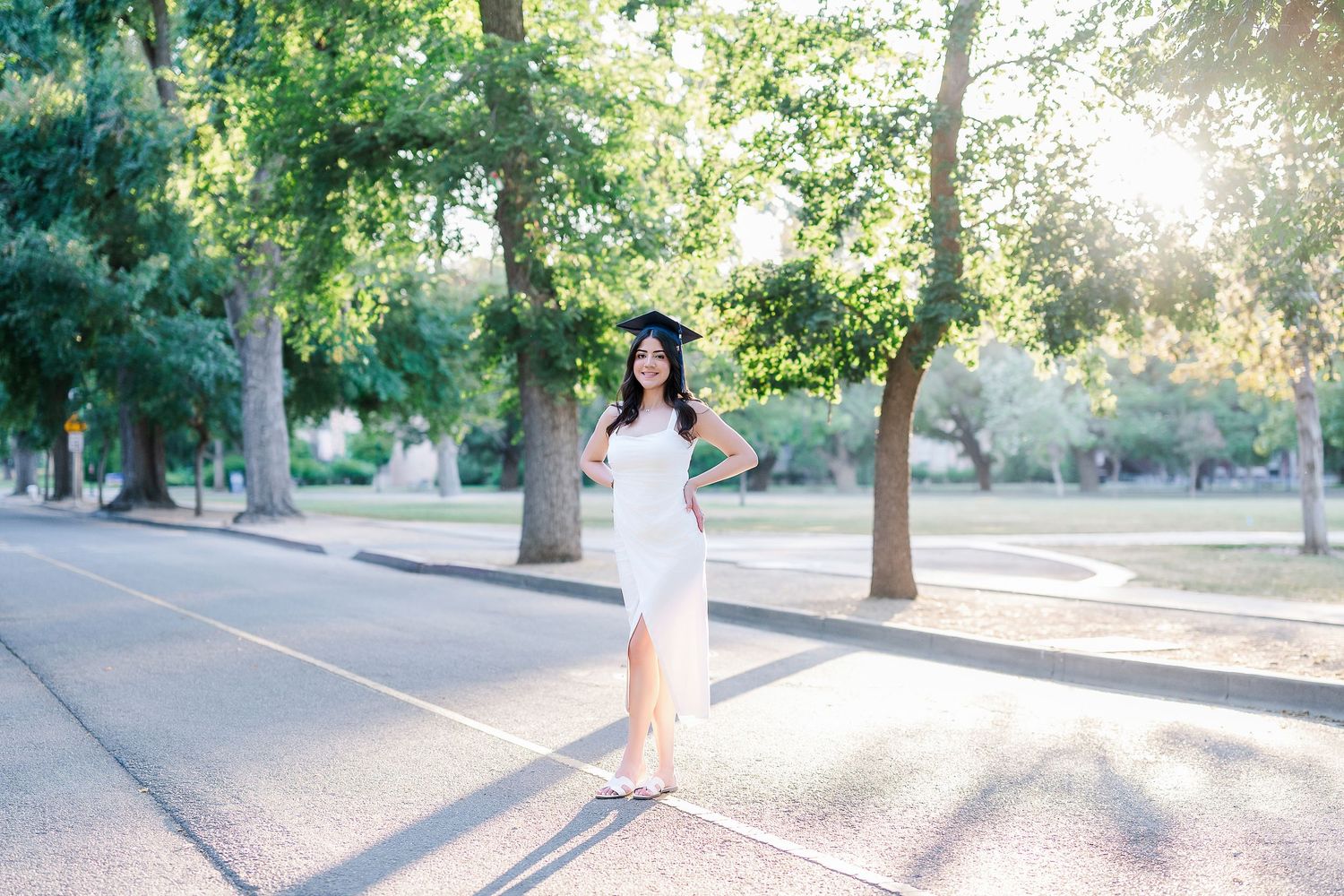 Graduates walking along a scenic tree-lined pathway during golden hour at UC Davis campus.