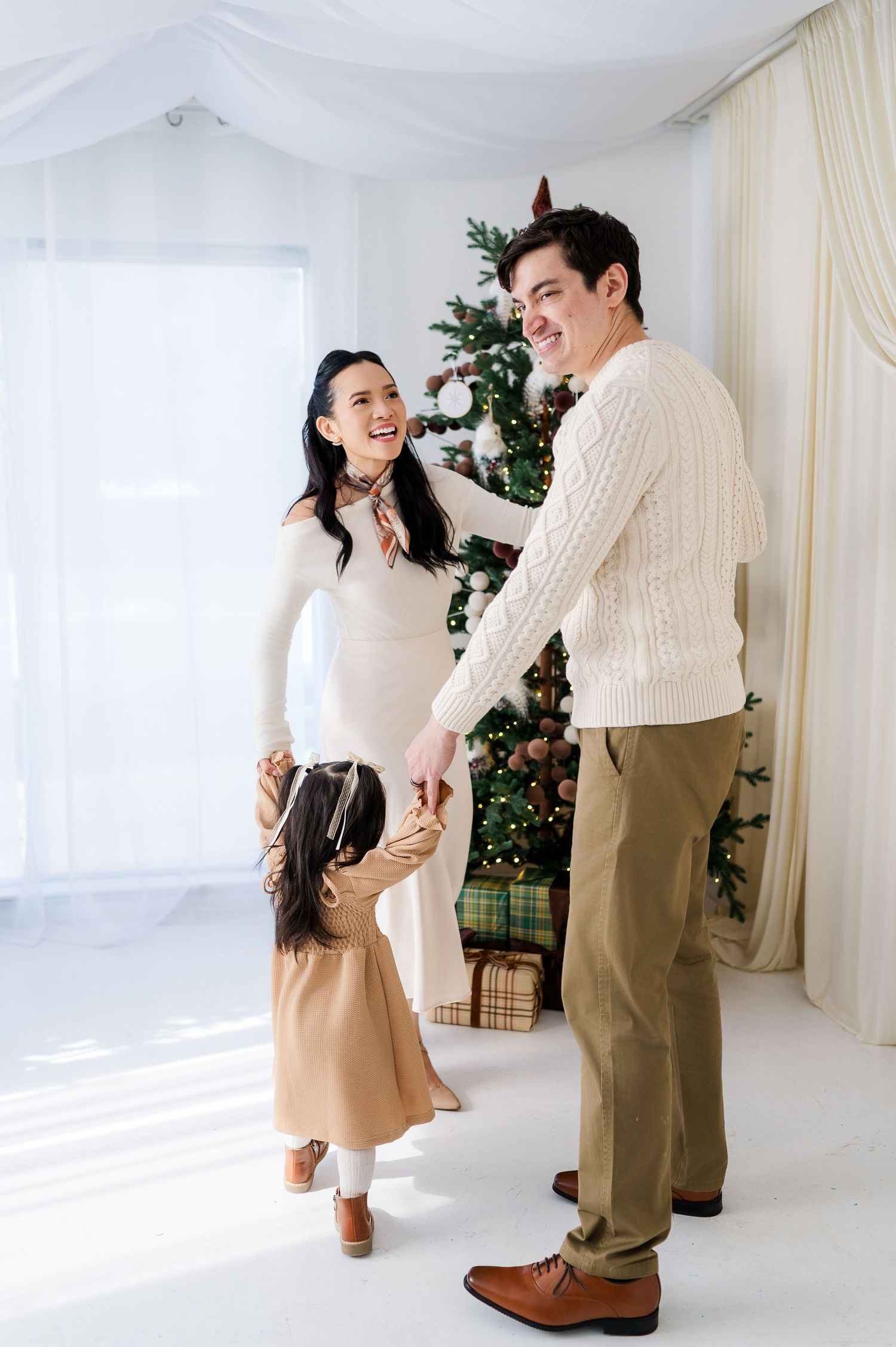 A couple shares a joyful moment dancing together in a bright studio with Christmas decorations in the background.