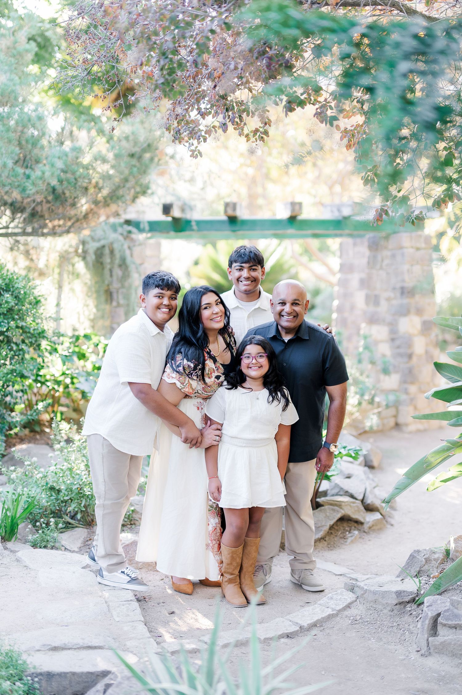 A family poses together in a garden setting wearing coordinated white and khaki outfits for outdoor portraits.