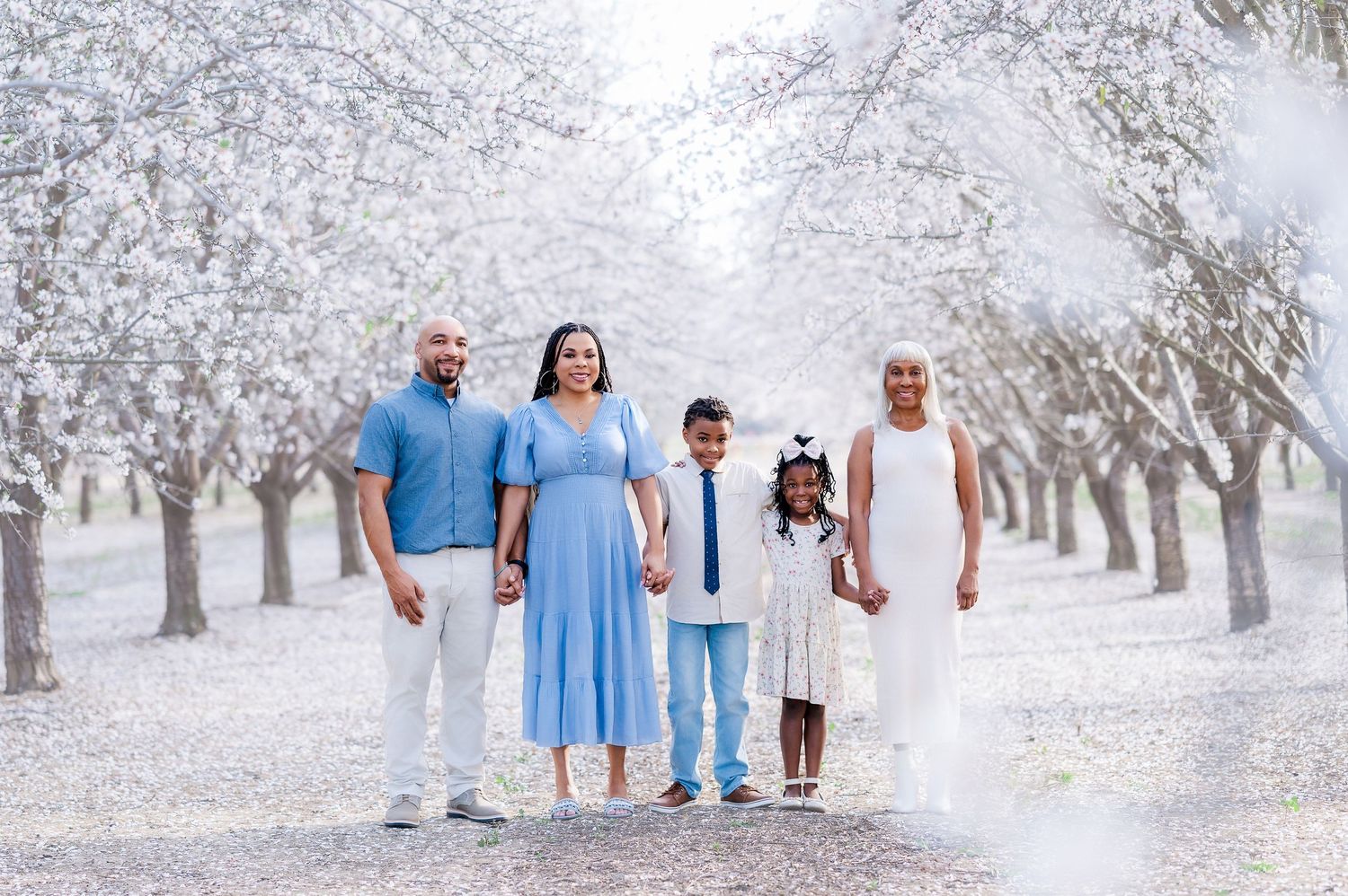 Family photoshoot in dreamy snow-covered almond orchard wearing coordinated winter outfits.
