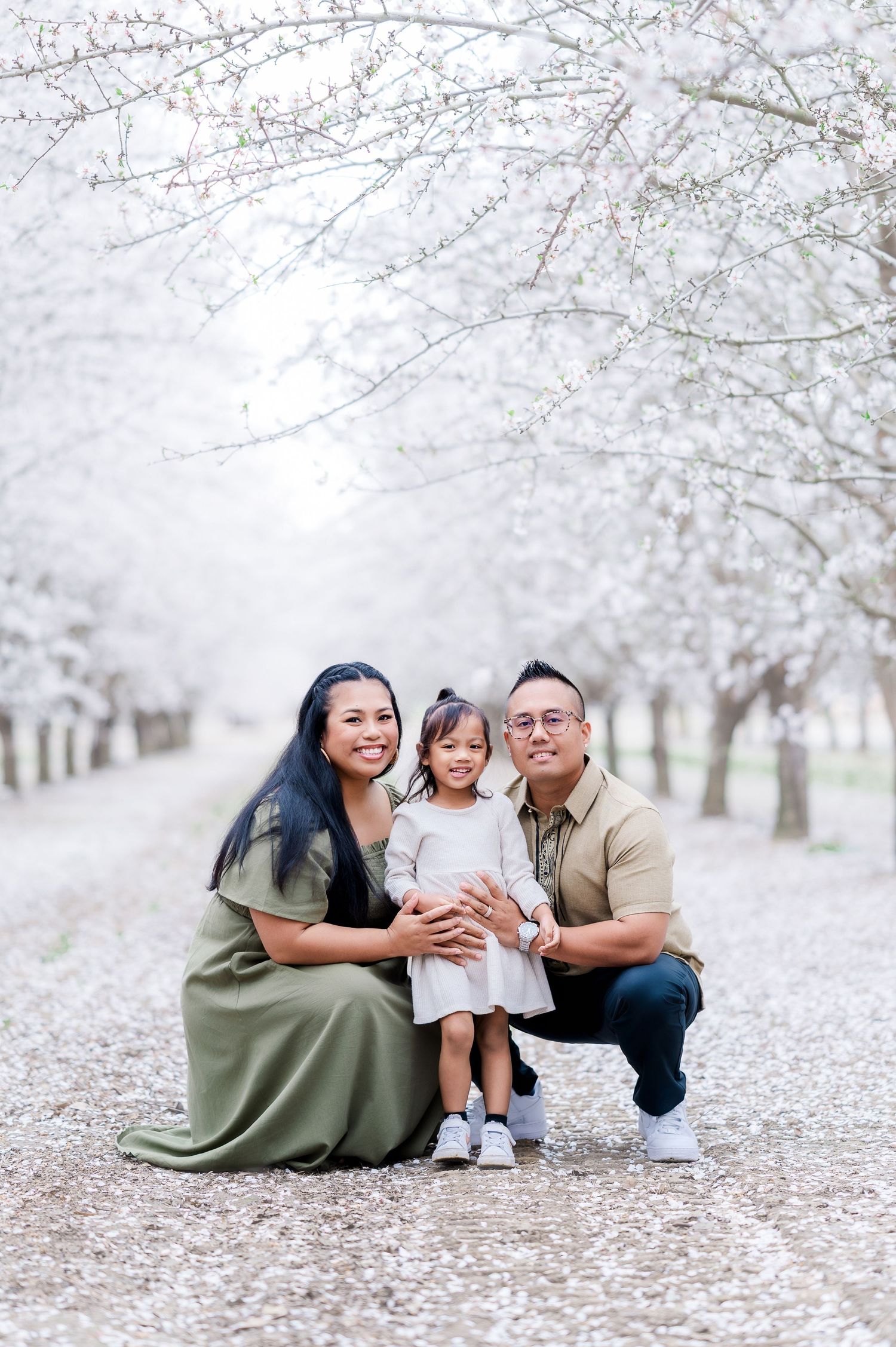 A family enjoys a tender moment together under blooming cherry blossom trees on a spring day.