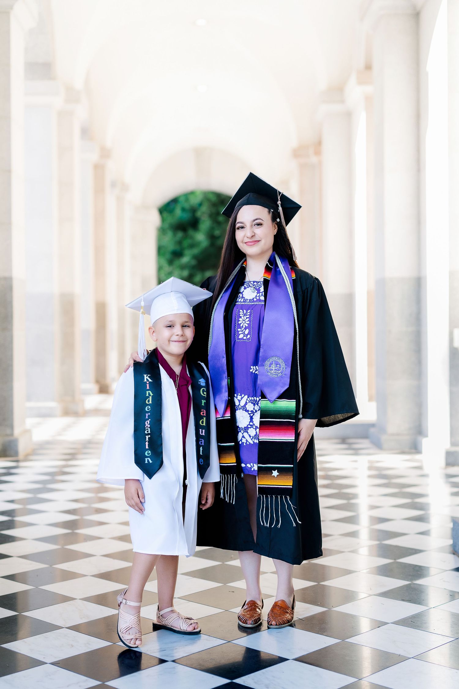 Graduates posing in an elegant colonnade with black and white checkered floor.