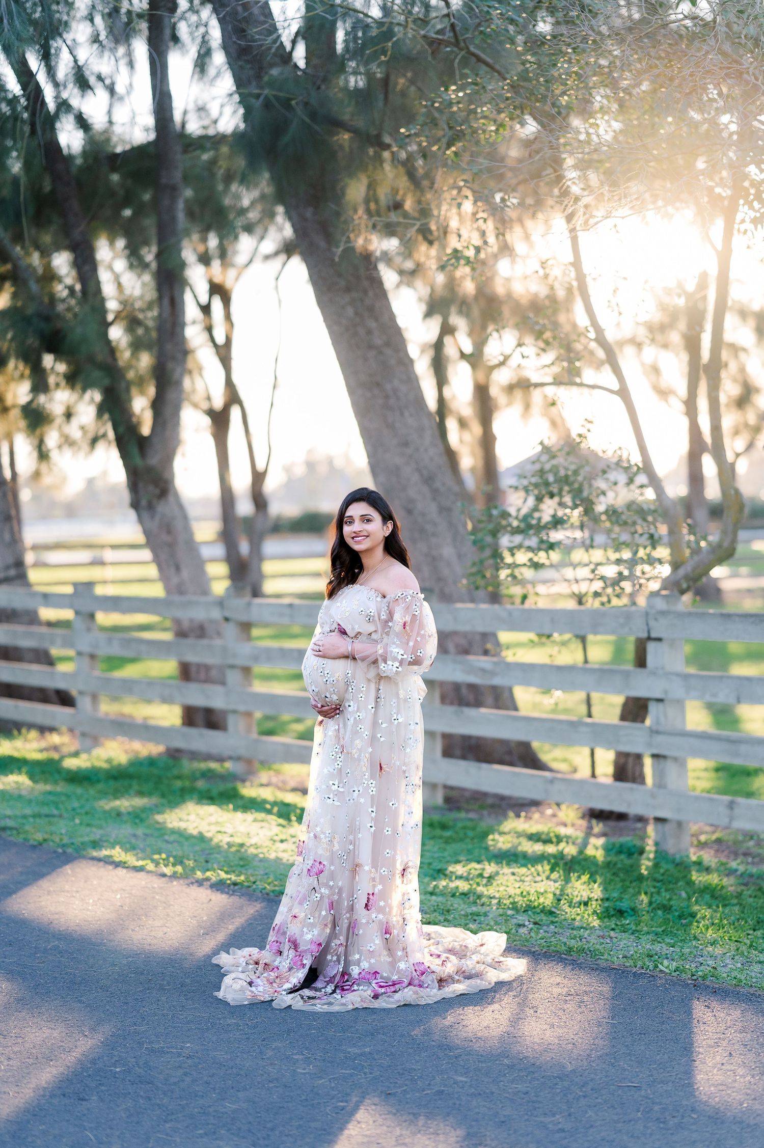 Ethereal maternity photoshoot in a park at sunset with a flowing floral lace gown.