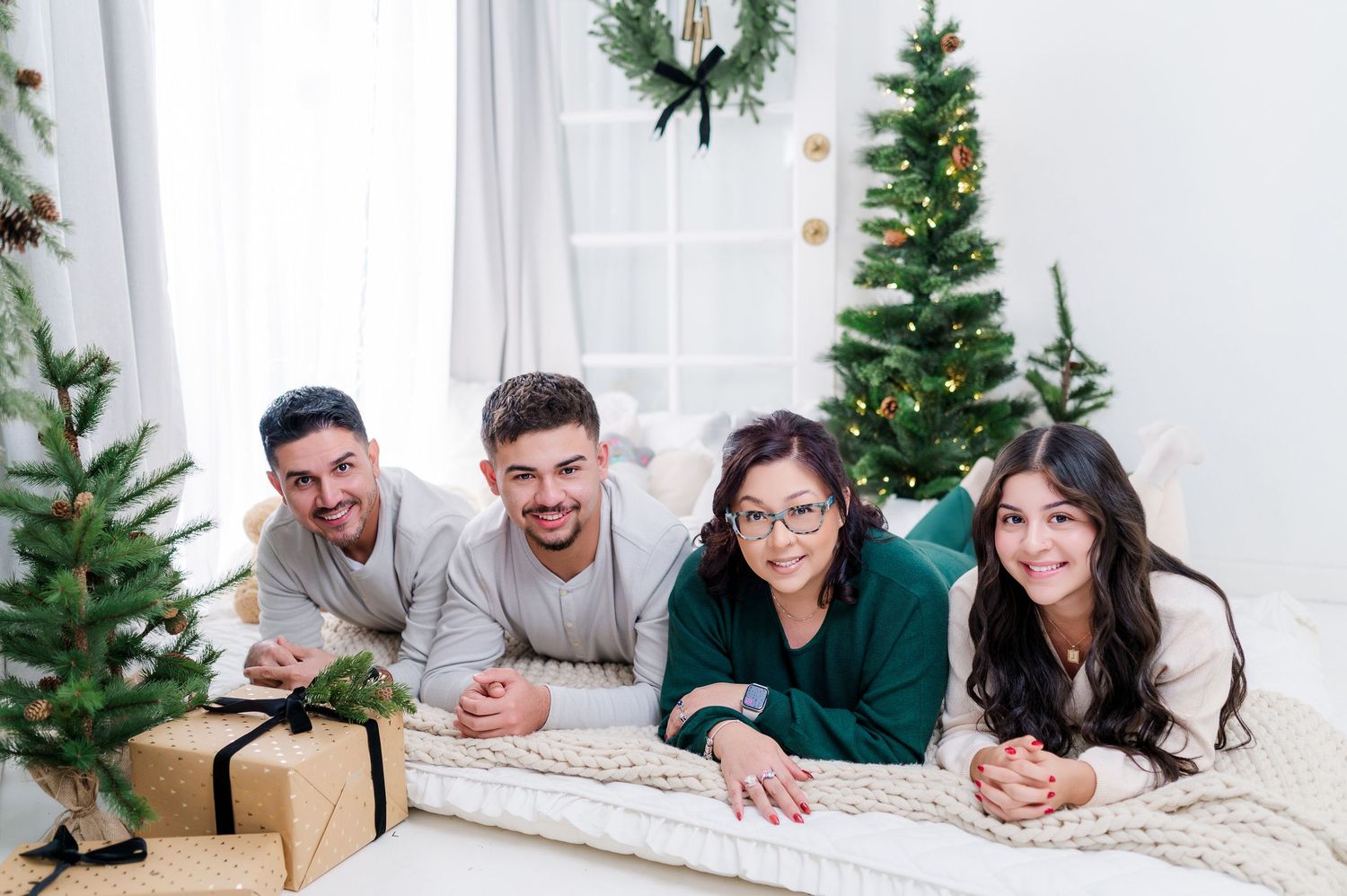 Family lying on carpet in front of Christmas tree during holiday photo session in white room.