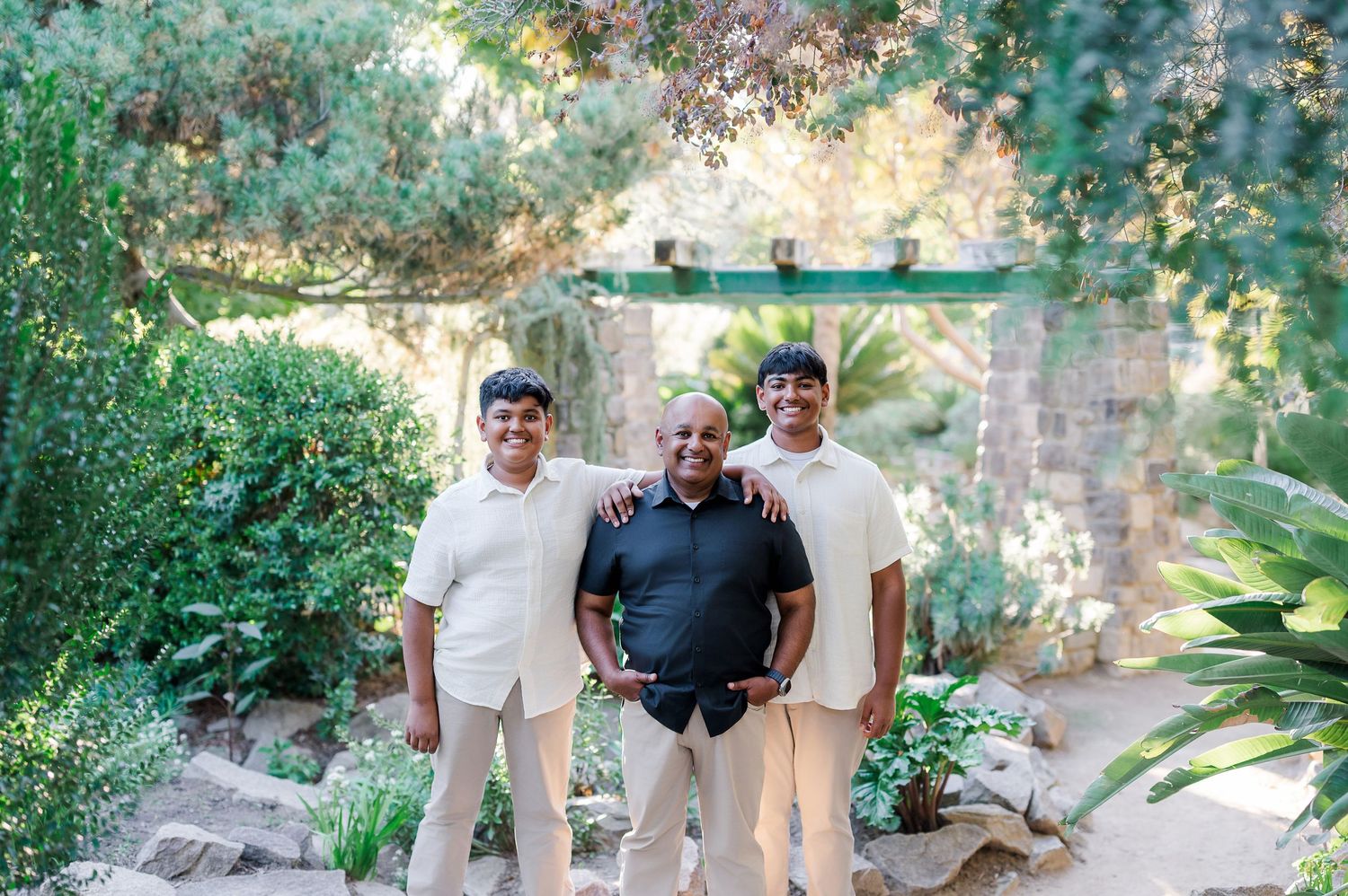 Family group poses together in front of a stone wall in an outdoor garden setting with lush greenery.