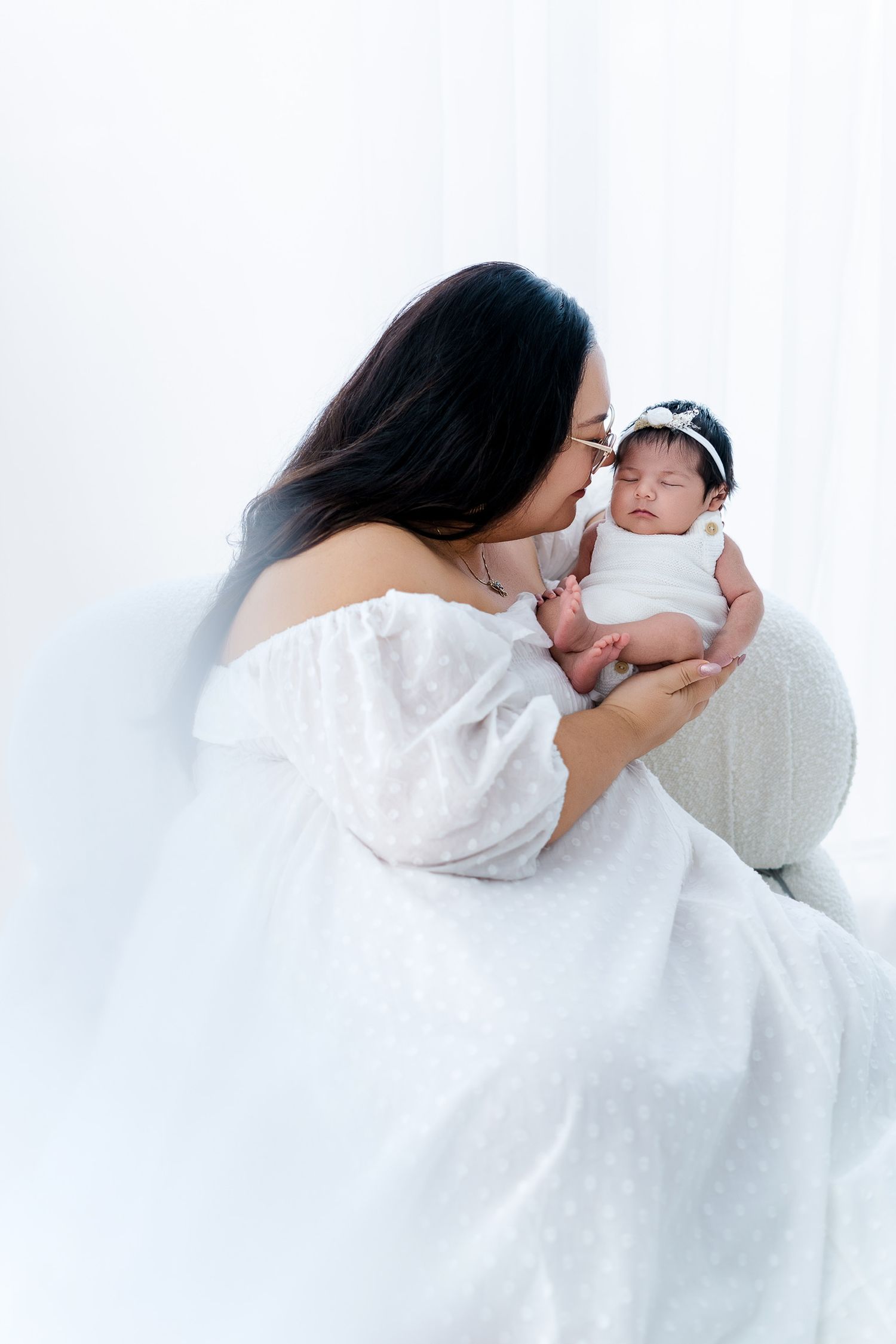 Tender moment between mother and newborn baby in white studio setting.