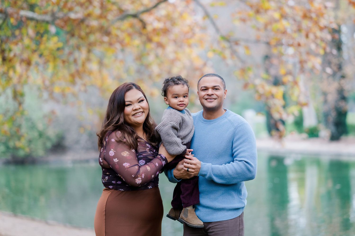 A couple shares tender moments during a fall photo session by a lake with autumn foliage in the background.