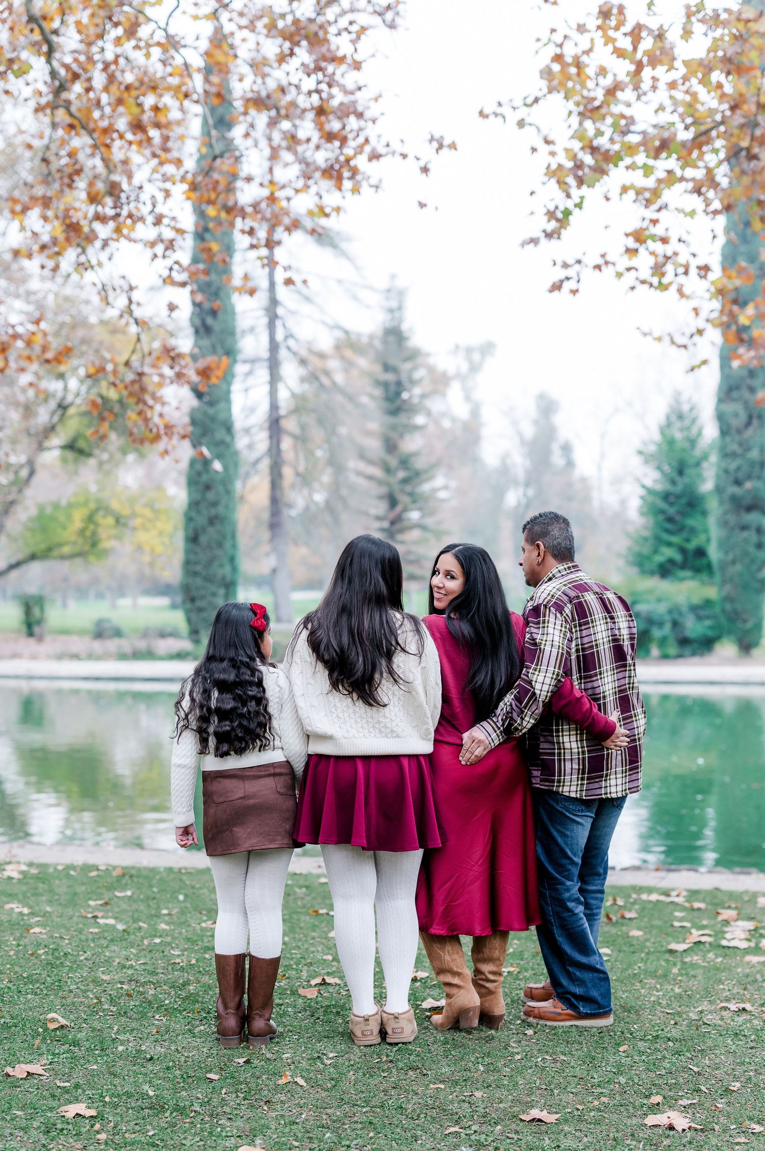 A group stands together in coordinated burgundy and white outfits by a tranquil pond on an autumn day.