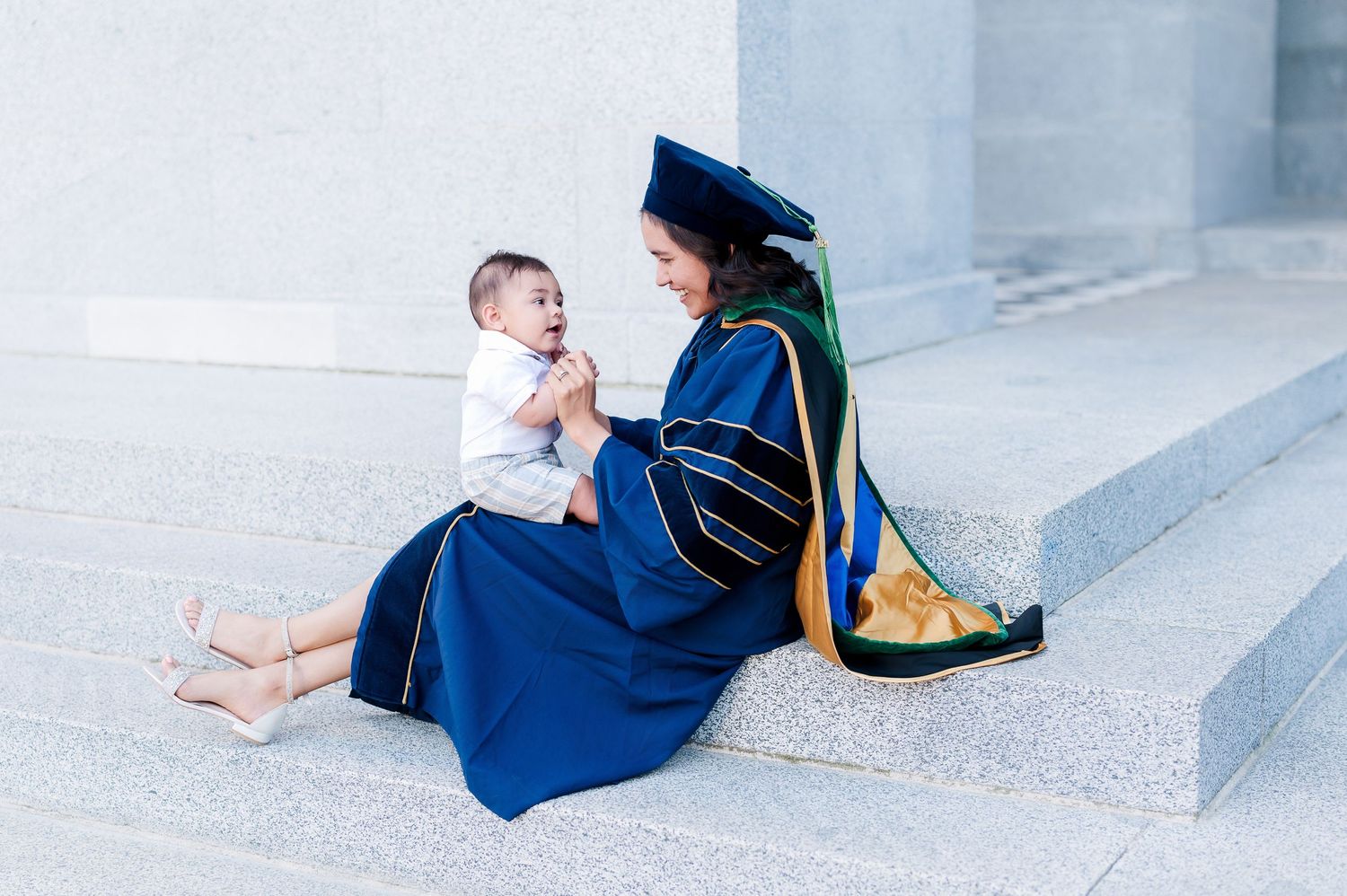 People in graduation attire sitting casually on light grey steps.