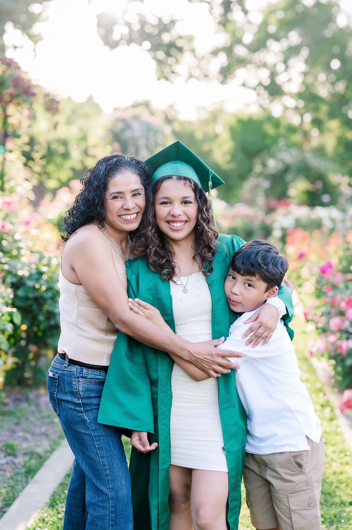 Graduate in green cap and gown smiles with family in a blooming garden during outdoor graduation photo session.