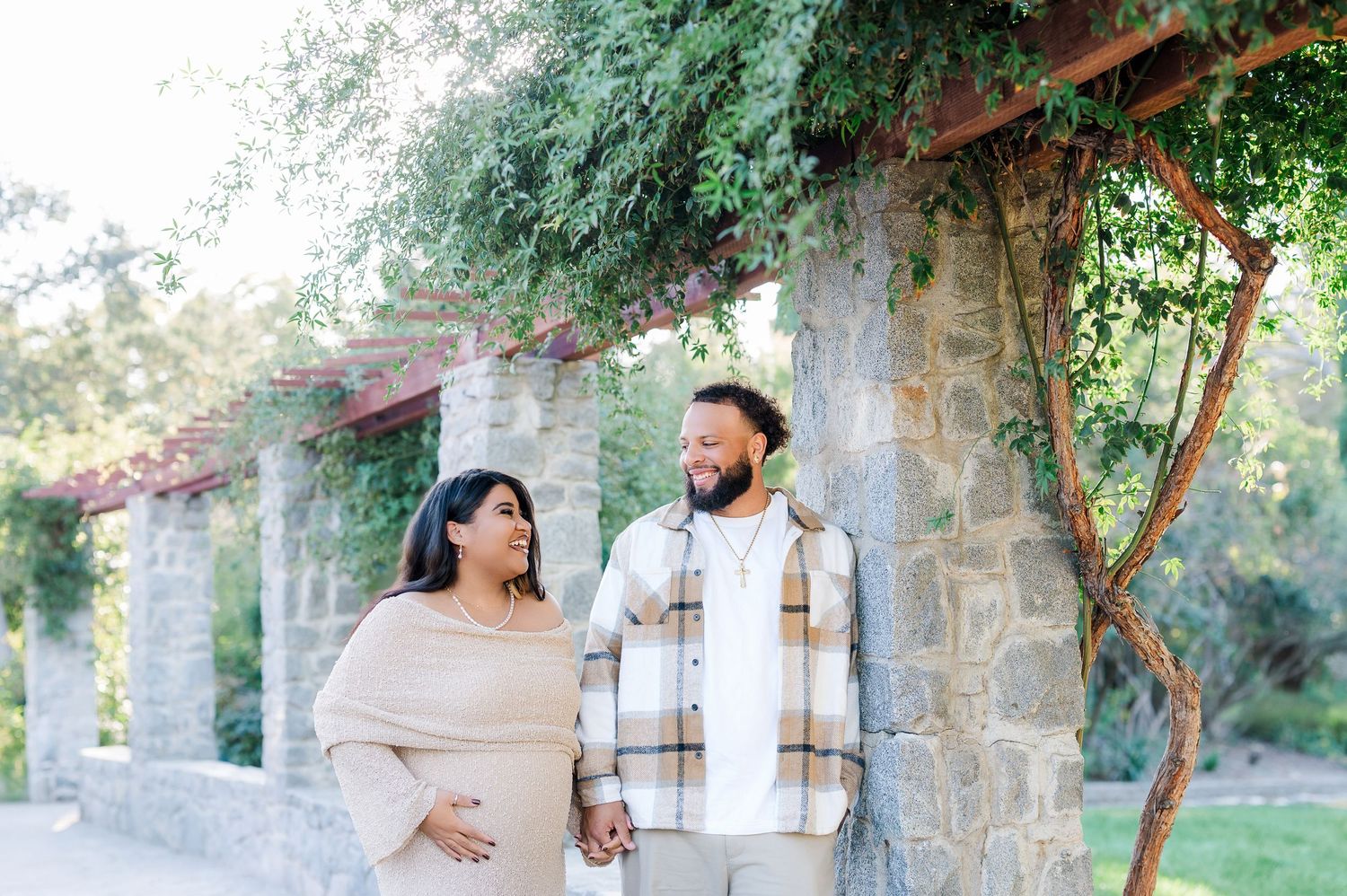 A couple poses together in a romantic garden setting with stone archways and lush greenery in the background.