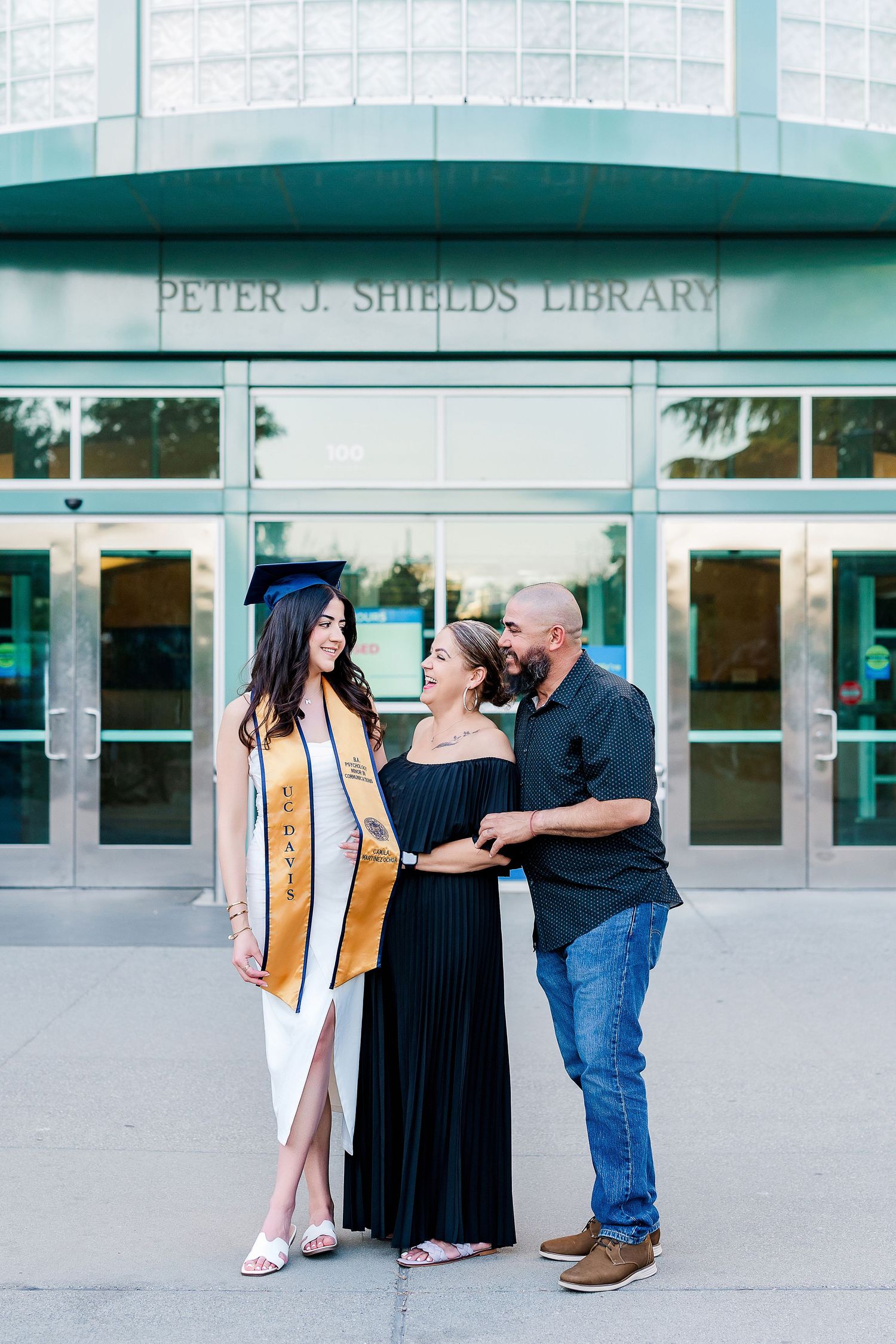 Family celebrating graduation outside Peter J. Shields Library with joyful embraces.