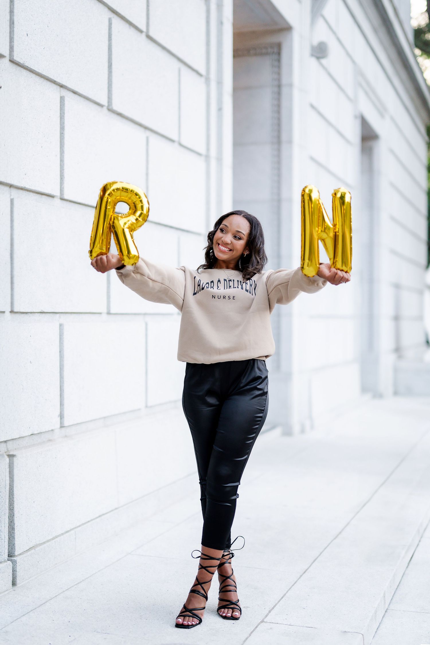 Person holding gold balloon letters against white architectural backdrop.