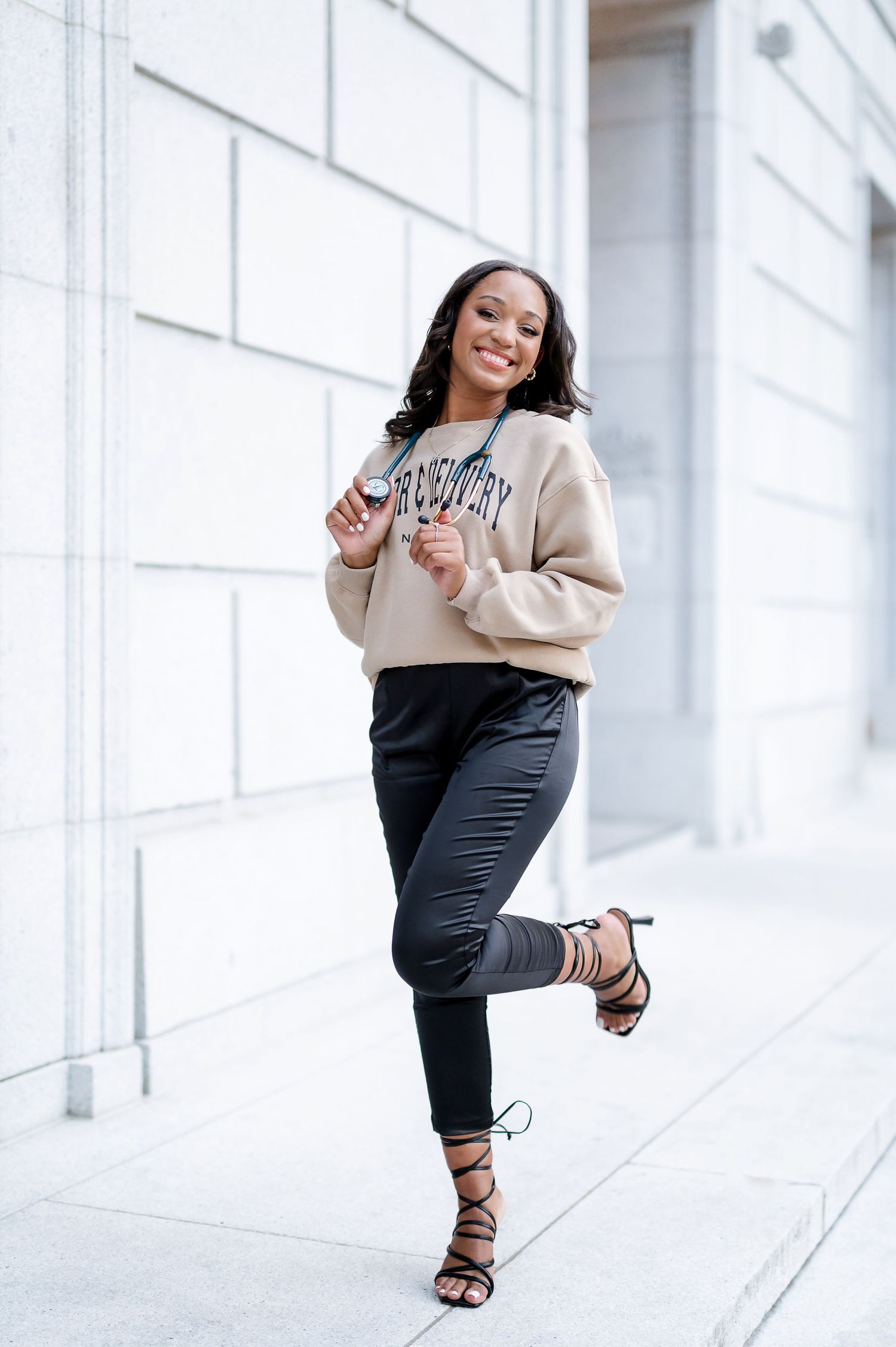 Stylish casual outfit photoshoot in beige sweater and dark pants against white building.