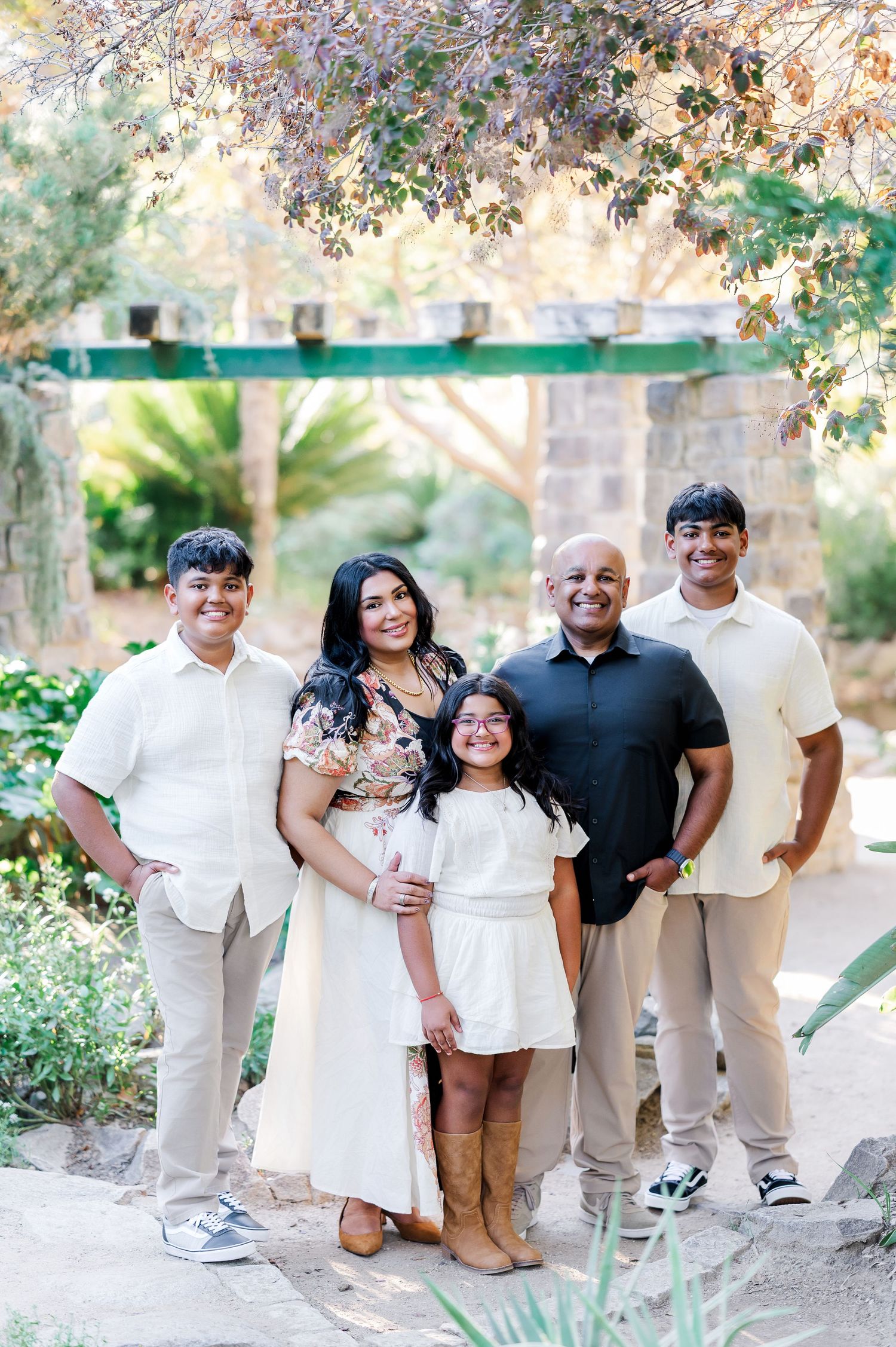 A family wearing coordinated white and beige outfits poses together outdoors in a natural setting for photos.