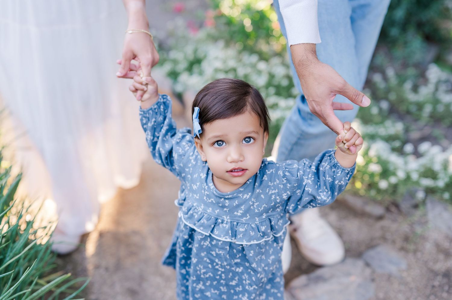 A child in a blue floral dress plays in a garden while holding sparklers during golden hour.