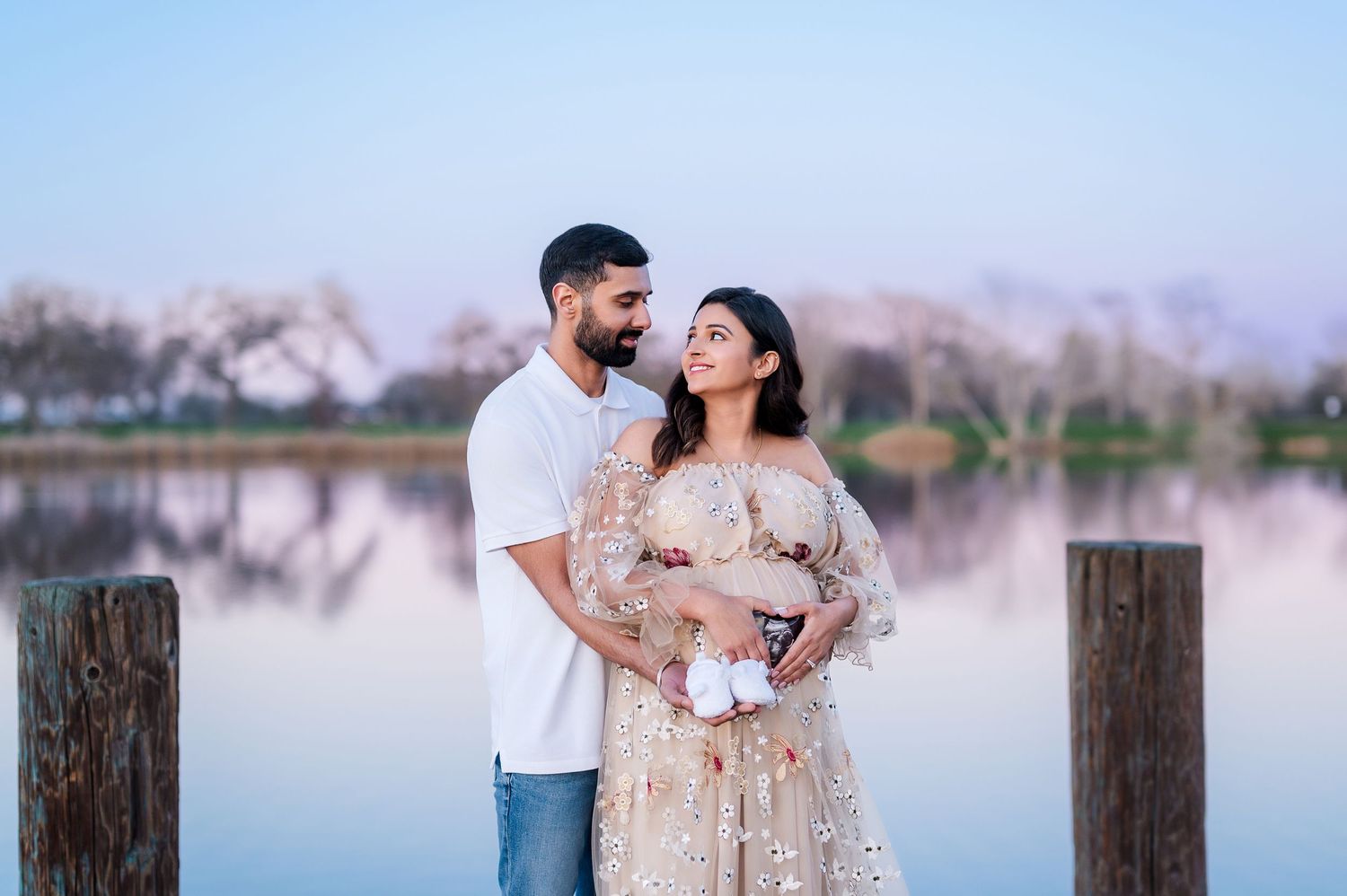 Maternity photos captured by a serene lake with soft pink sunset tones in the background.