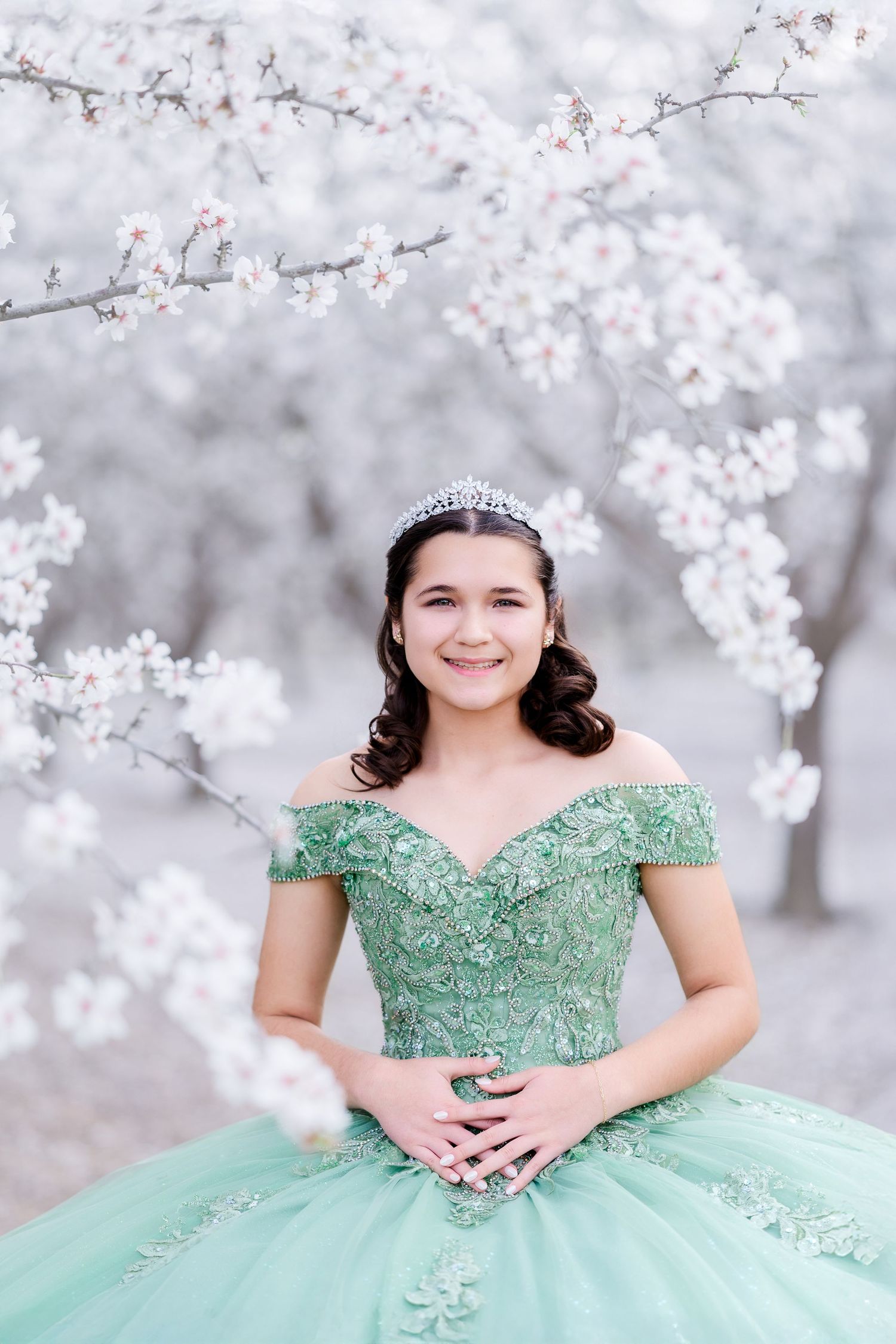 A mint green quinceanera ball gown with off-shoulder design photographed among delicate cherry blossoms.