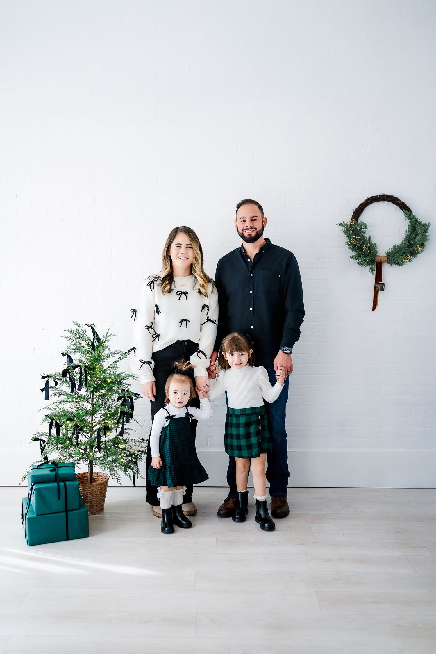 Holiday family portrait with Christmas tree and children in matching plaid skirts.