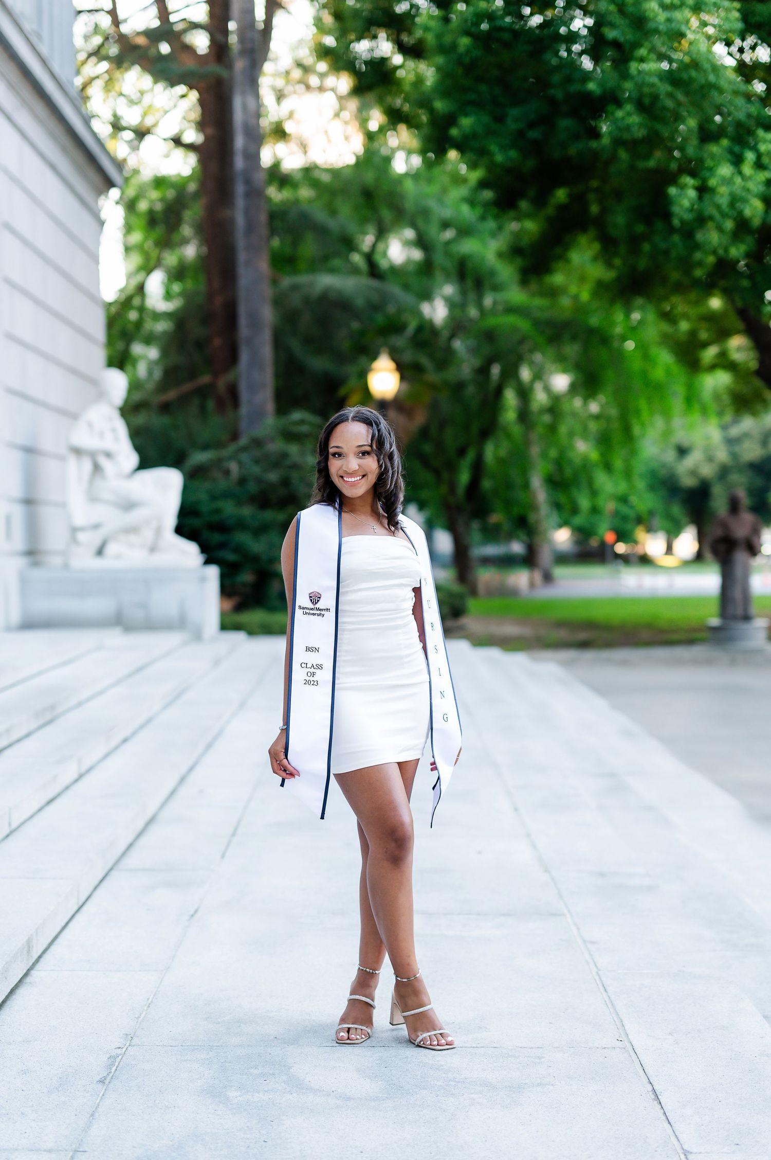 Professional photoshoot in white outfit against architectural backdrop outdoors.
