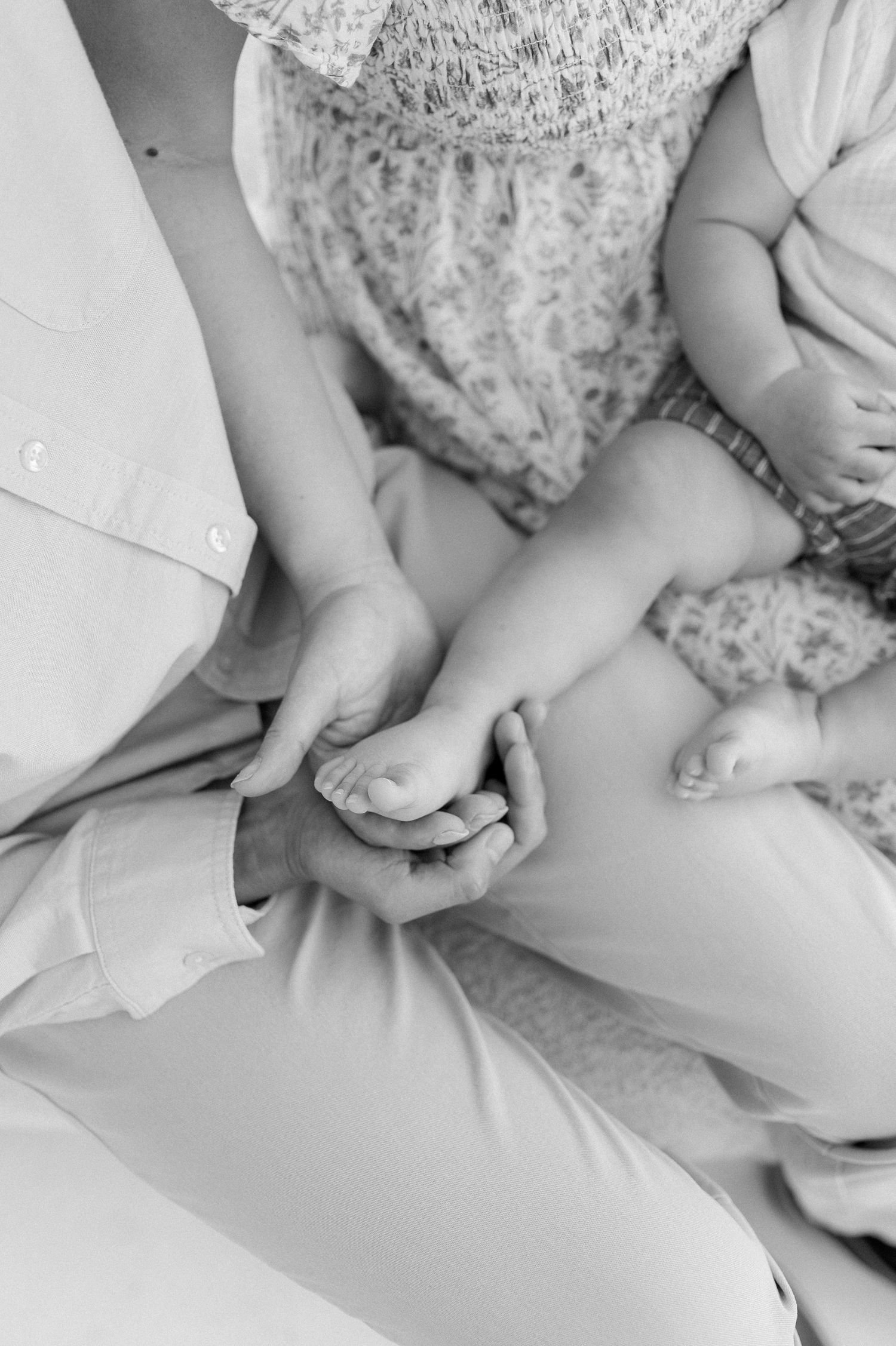 Black and white photo of parents holding their baby's tiny feet and hands, a tender family bonding moment.