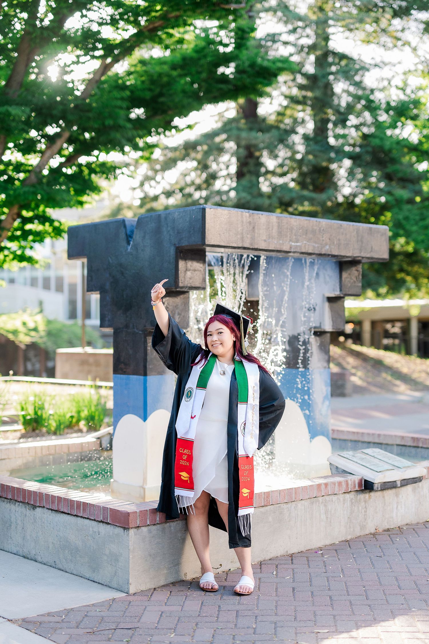 Graduate in cap and gown posing on outdoor brick steps with decorative concrete walls.