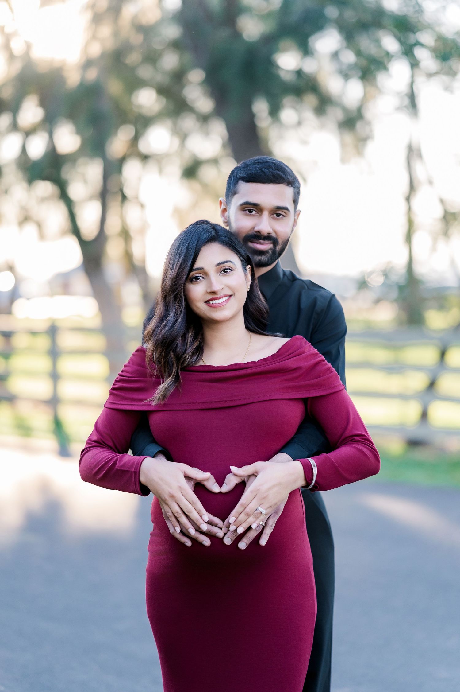 Romantic maternity photos of couple in burgundy dress and black outfit posing together outdoors.