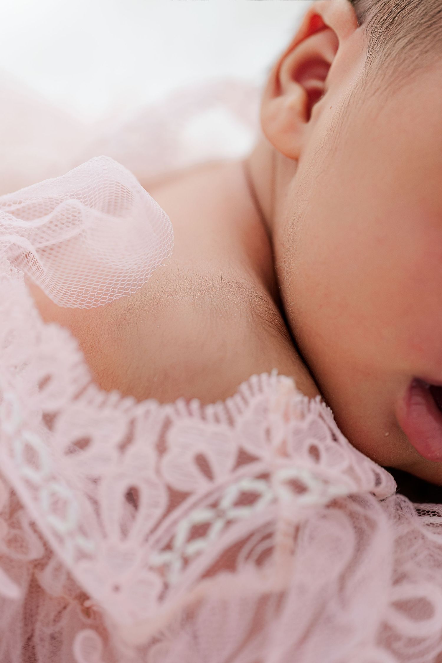 Close-up of a sleeping newborn baby wearing a delicate pink lace dress, soft natural light highlighting their peaceful expression.