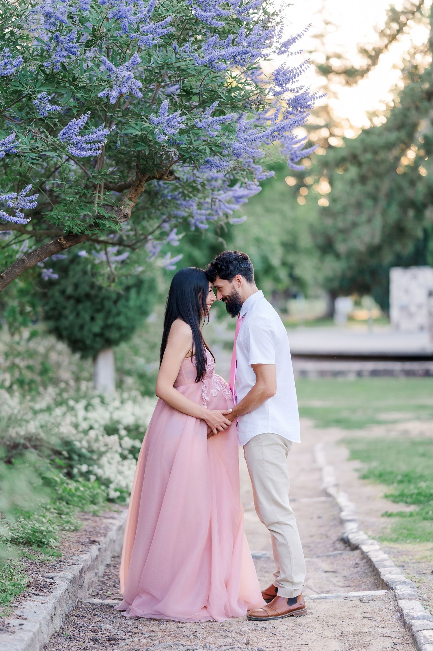 Romantic couple shares tender moments under blooming purple wisteria flowers on a garden path at sunset.