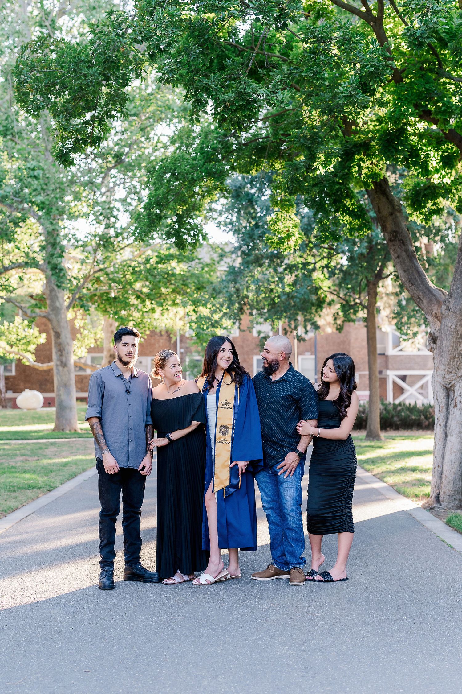 Group of family and friends gather on tree-lined path for graduation celebration photos.