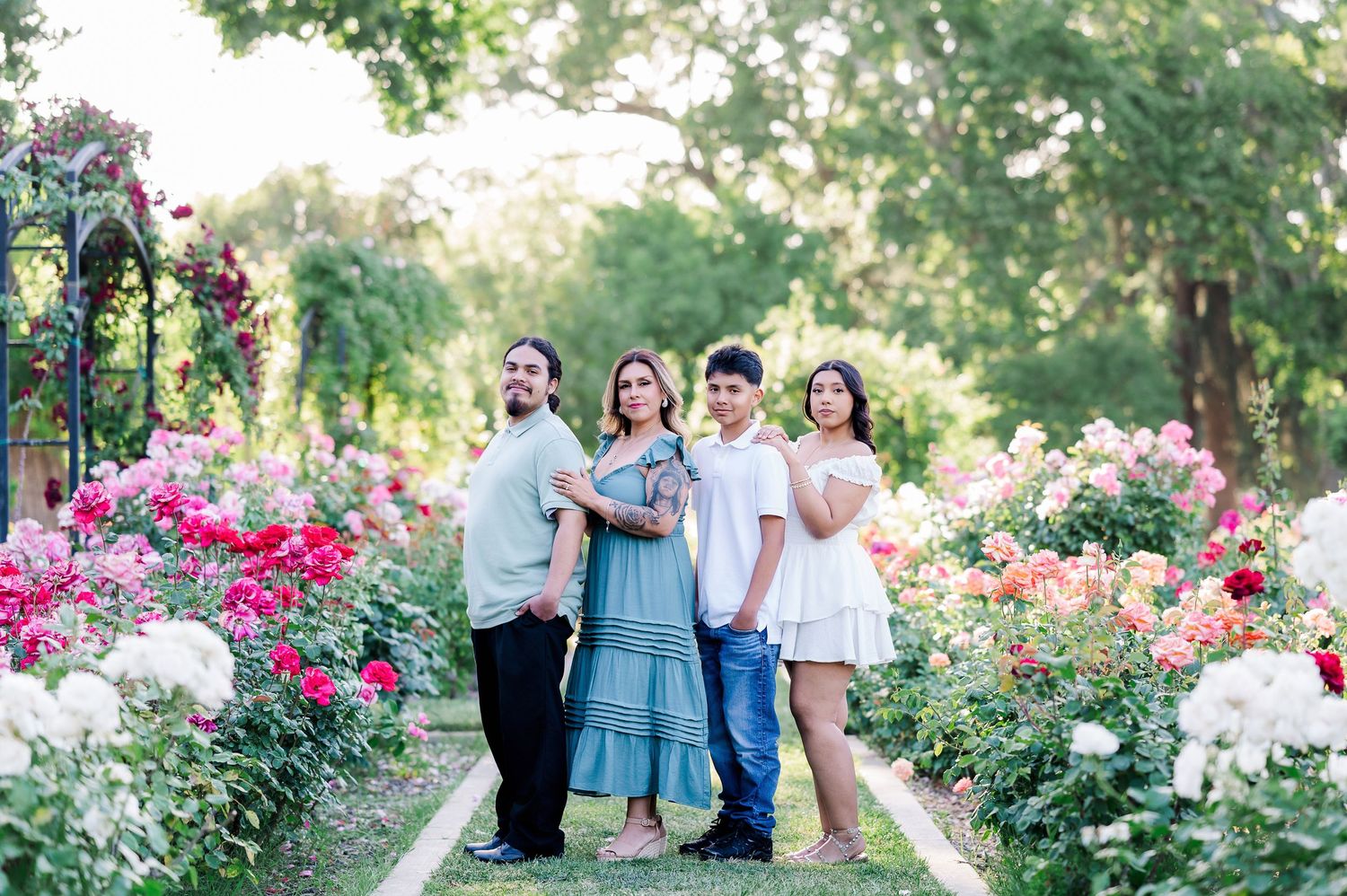 A family poses together on a garden pathway surrounded by vibrant pink and white roses.