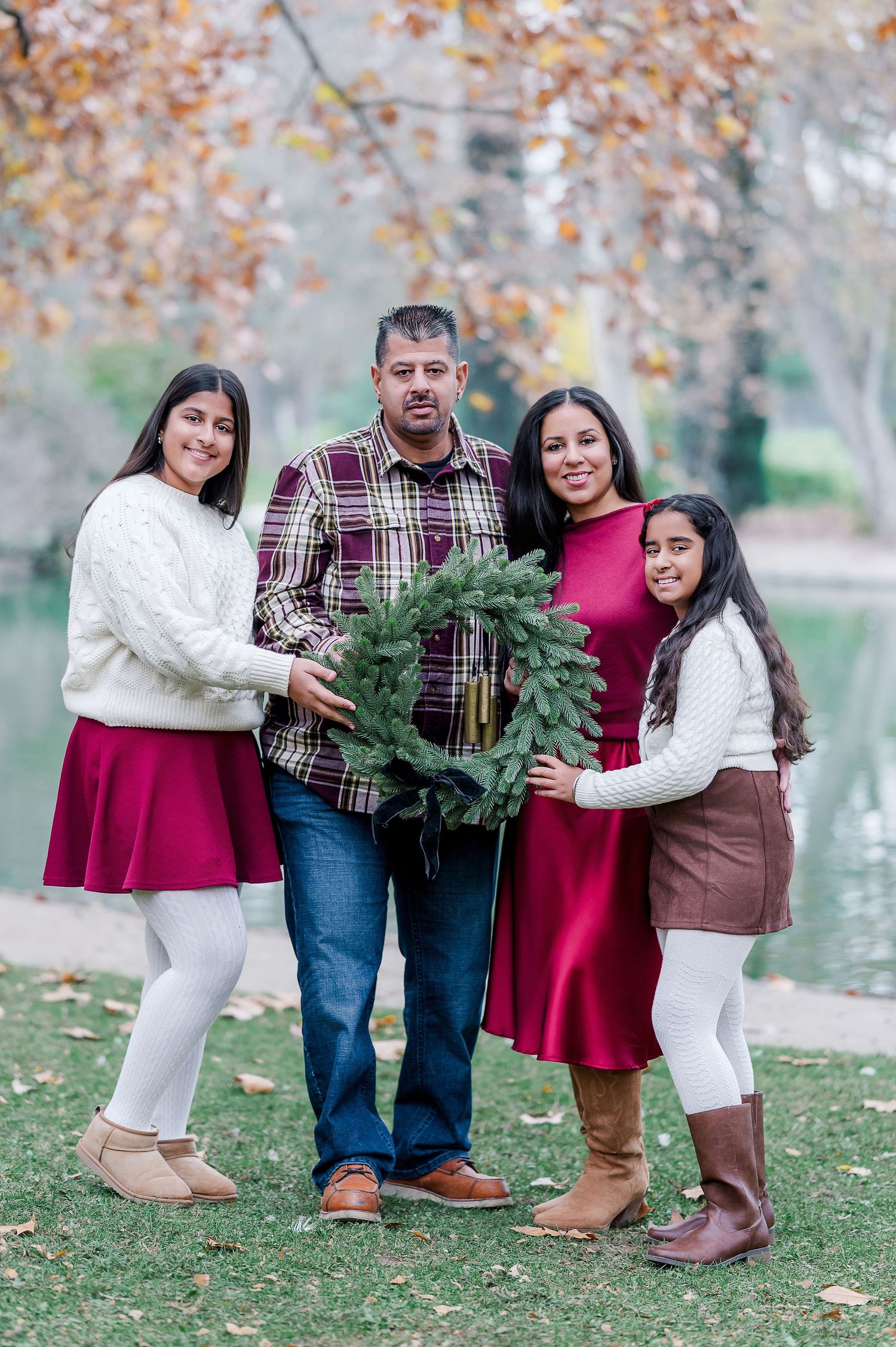 A group poses together outdoors in coordinated burgundy and white outfits while holding a small Christmas tree.